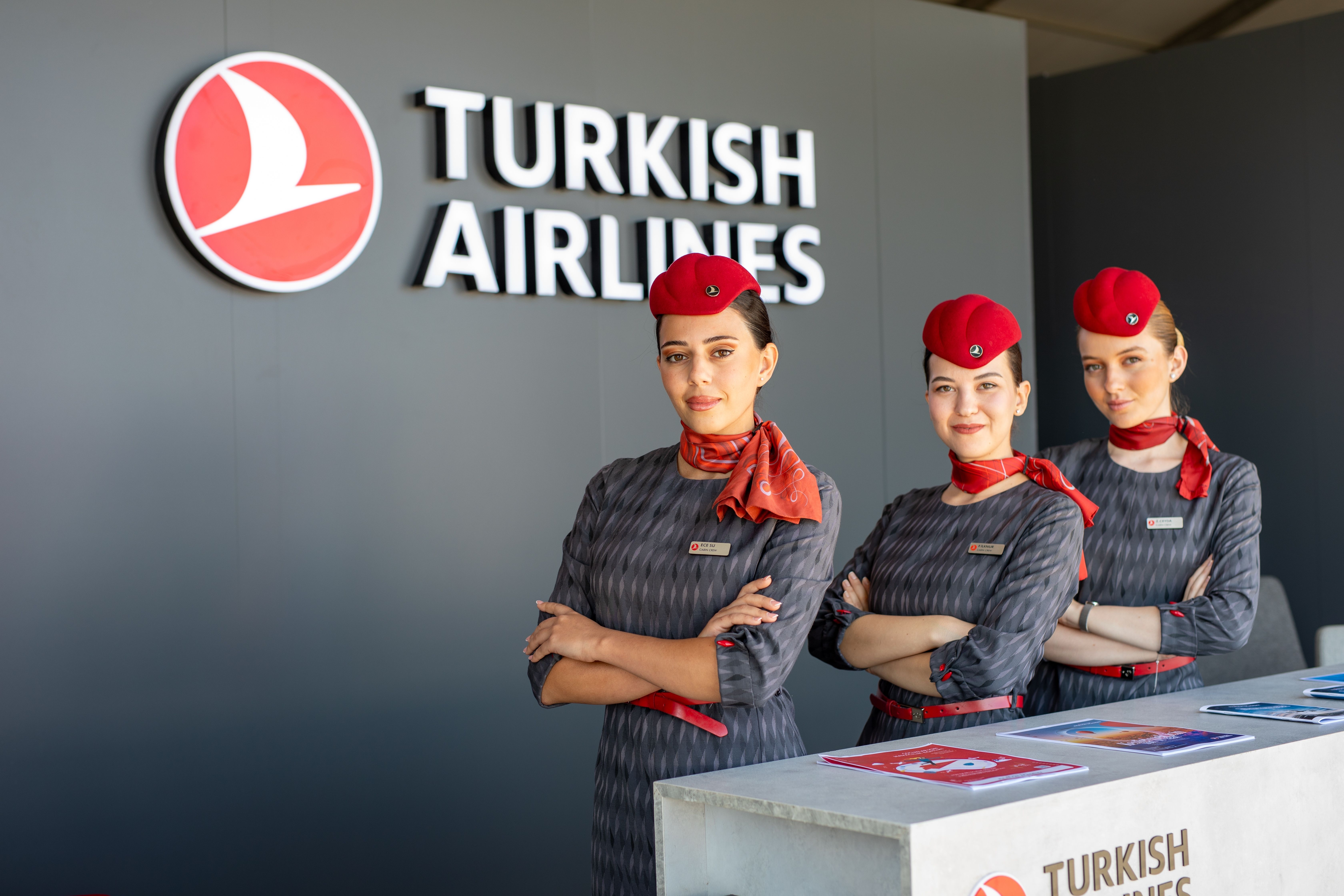 Three Turkish Airline cabin crew members standing near a departure gate desk.