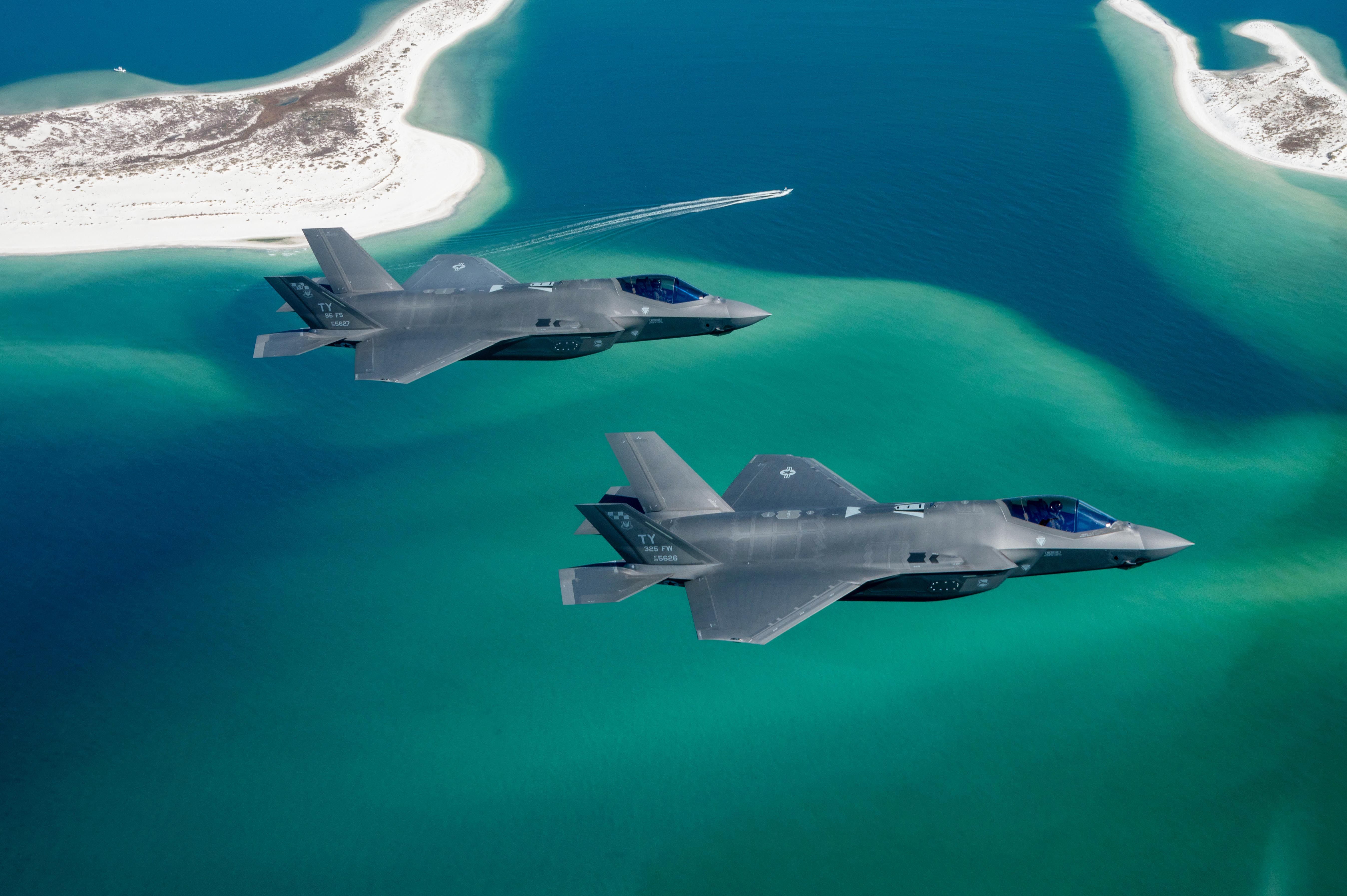 Two fighter jets flying over water.