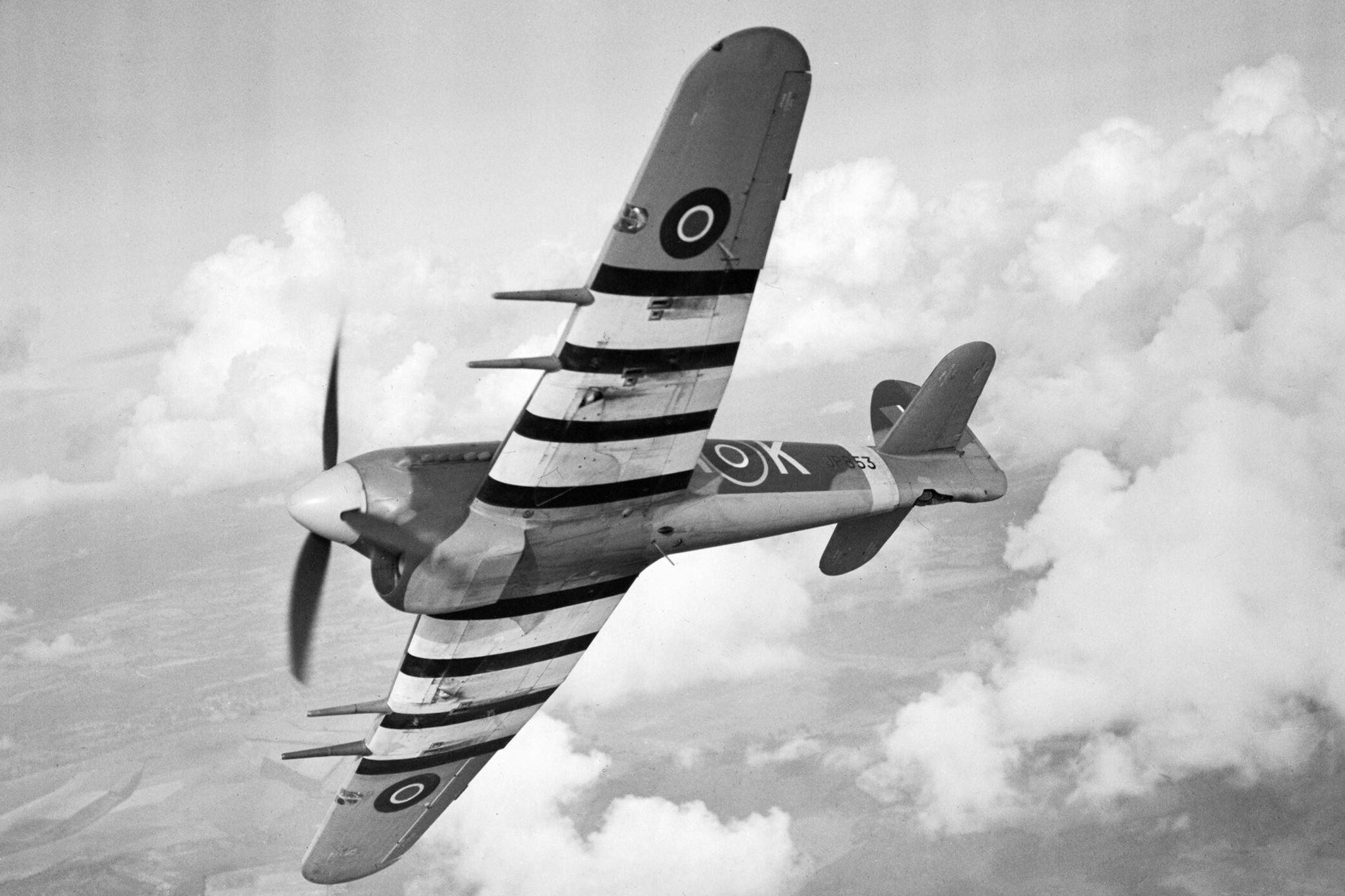 A black and white photo of a Hawker Typhoon flying in the sky.