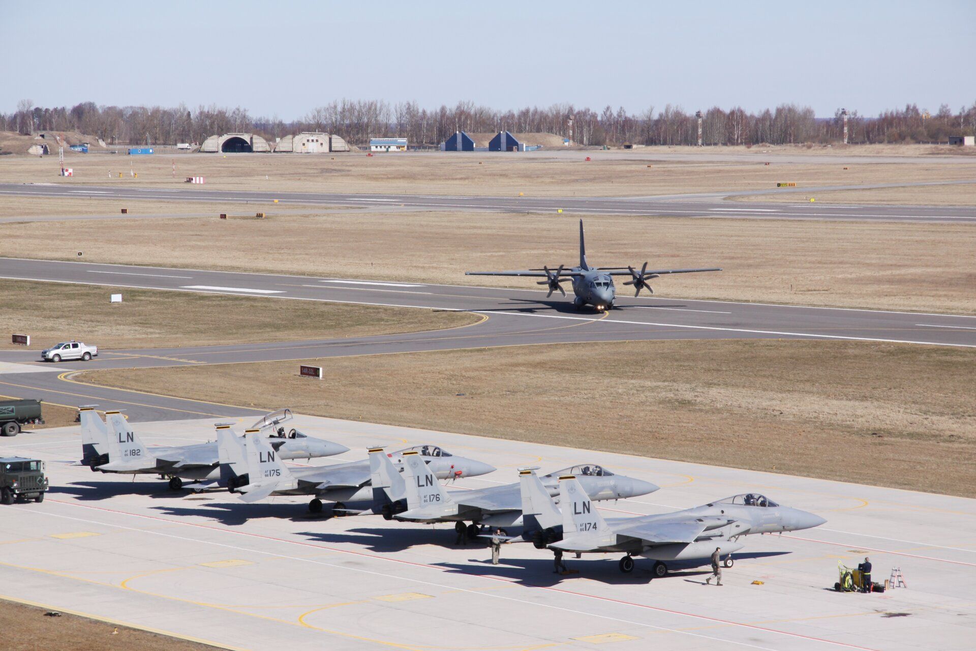 A LTAF Alenia C-27J Spartan and several fighter jets on a military airport apron.