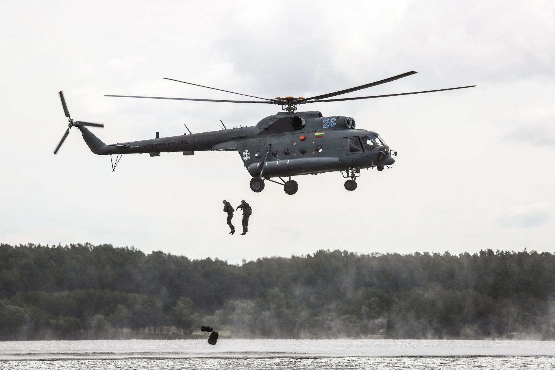 A LTAF Mil Mi-8 hovering over water as military personnel jump out.