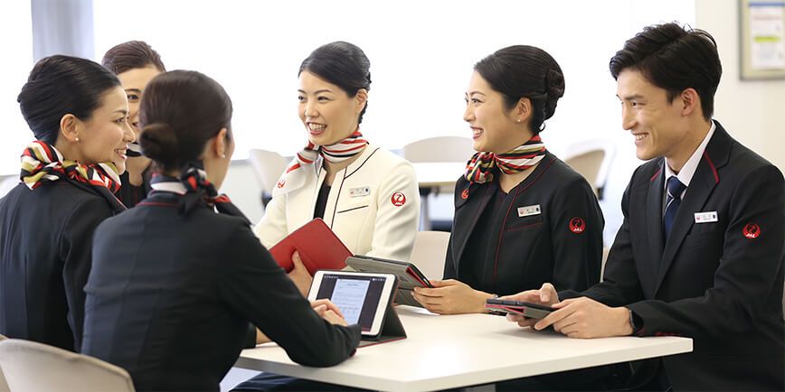 Several Japan Airlines Cabin crew around a table for a briefing.