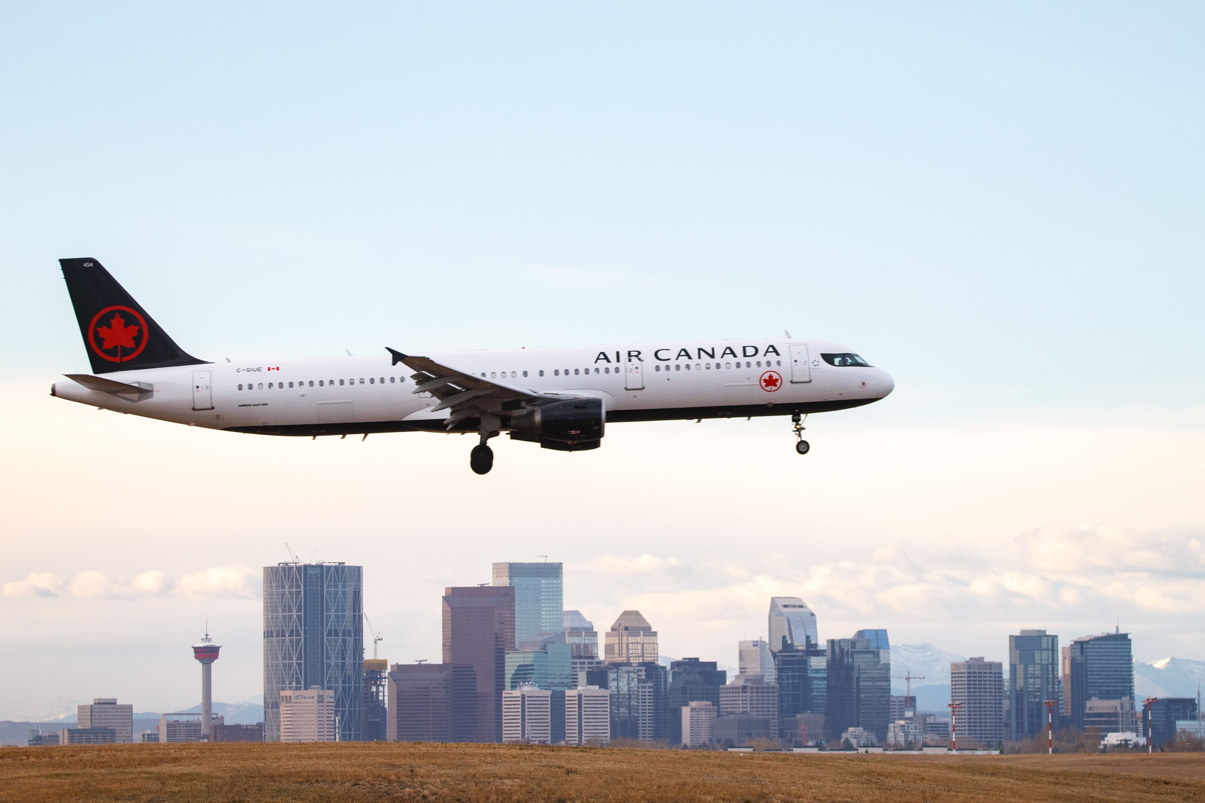 An Air Canada Airbus A321 flying in the sky with a city skyline in the background.