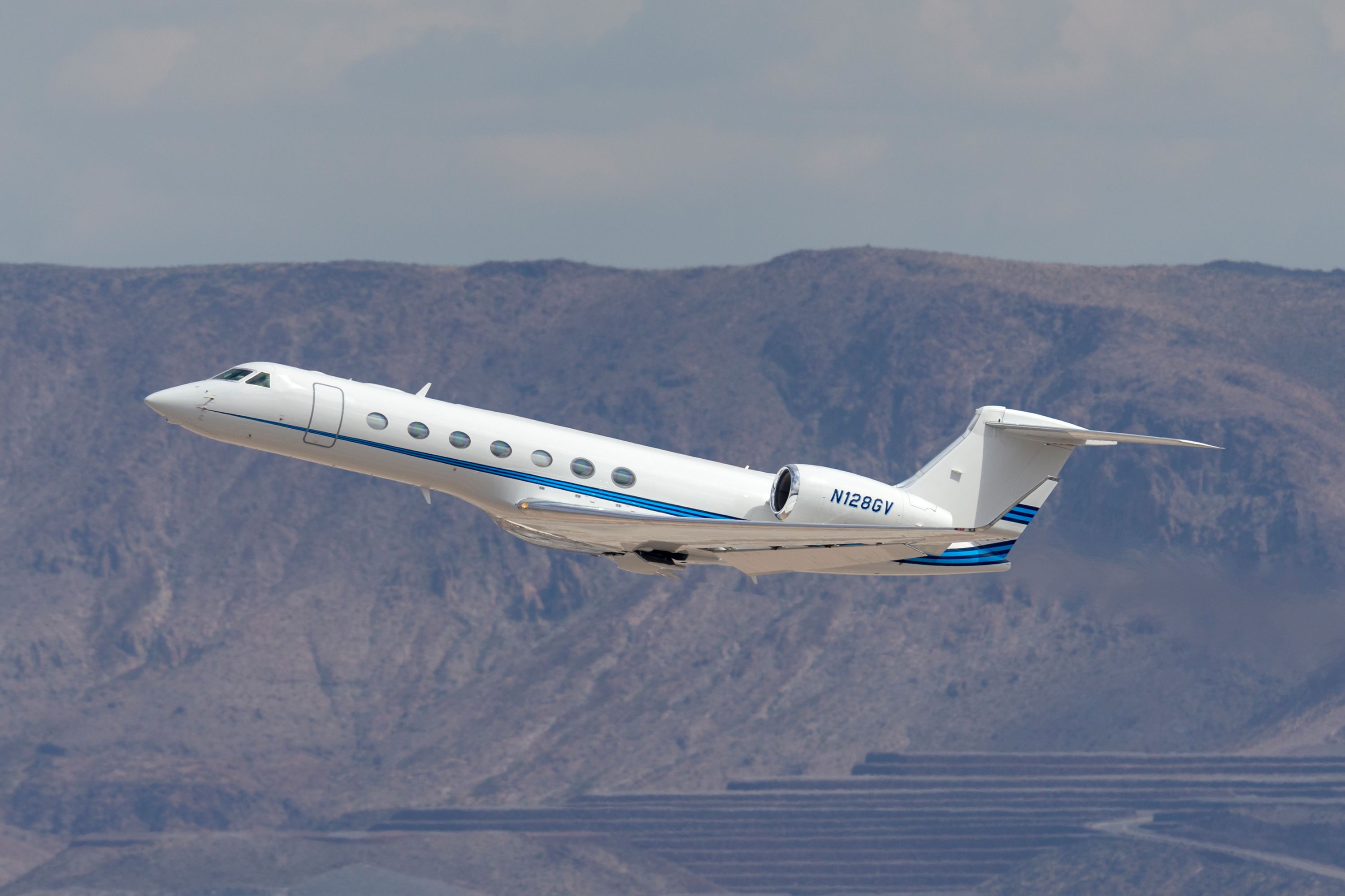 A Gulfstream G-550 luxury business jet just after take off with mountains in the background.