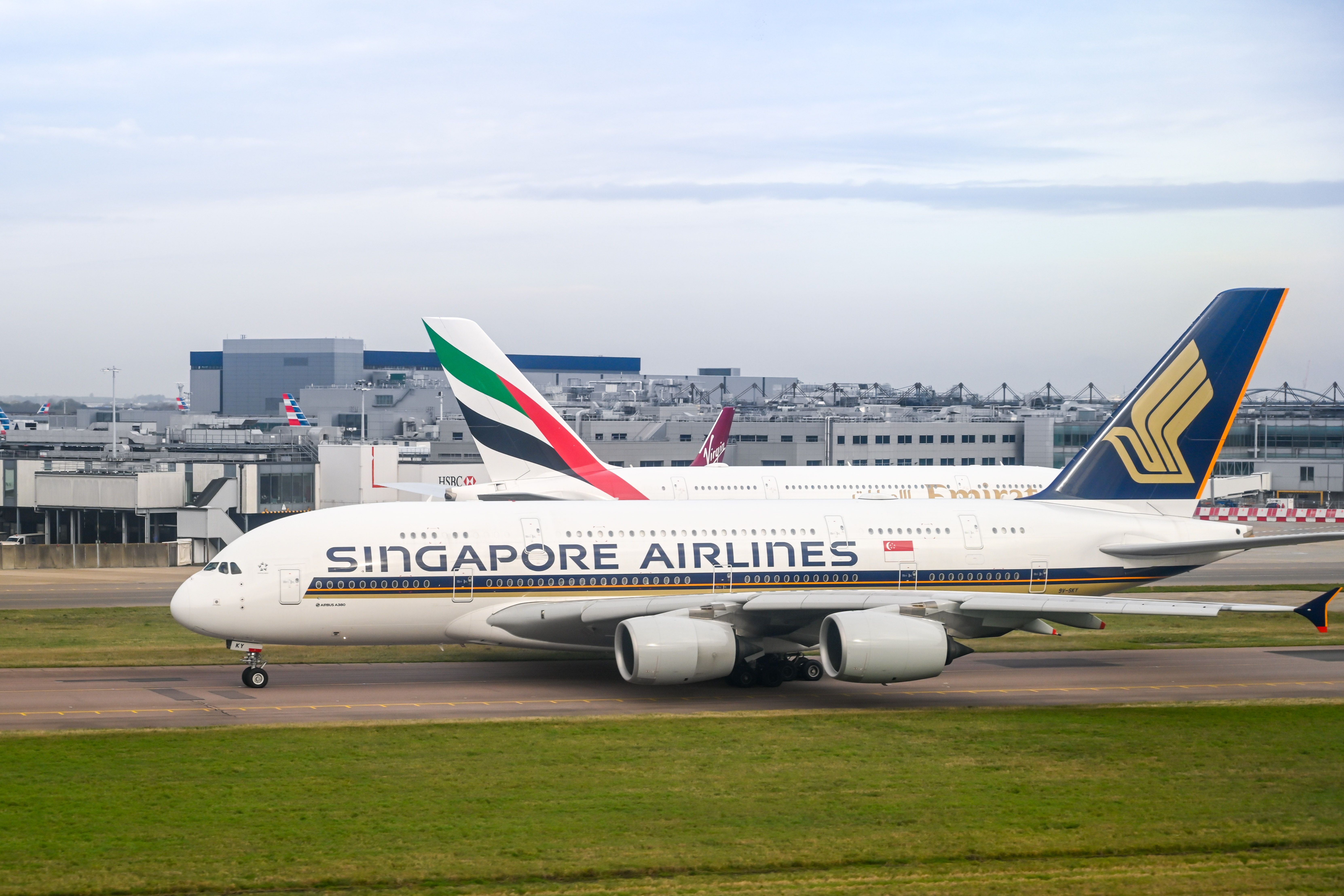 Singapore Airlines Airbus A380 and Emirates A380 stand on the apron of London Heathrow Airport.