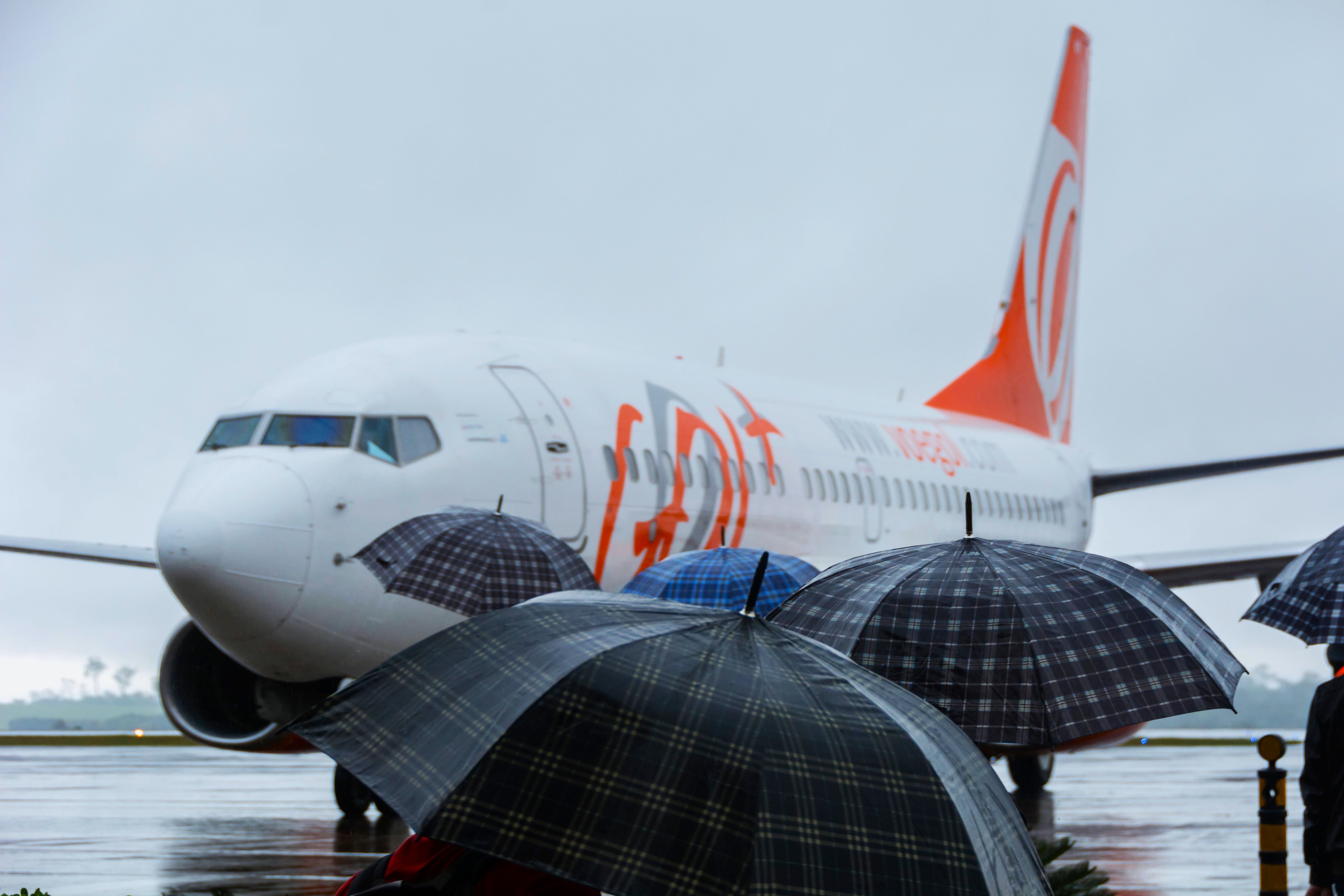 shutterstock_1869465385 - Foz do Iguaçu, Paraná - Brazil - August 20, 2016: Passengers boarding with umbrellas on a rainy day at Foz do Iguaçu airport. Gol Airlines airplane in the terminal.