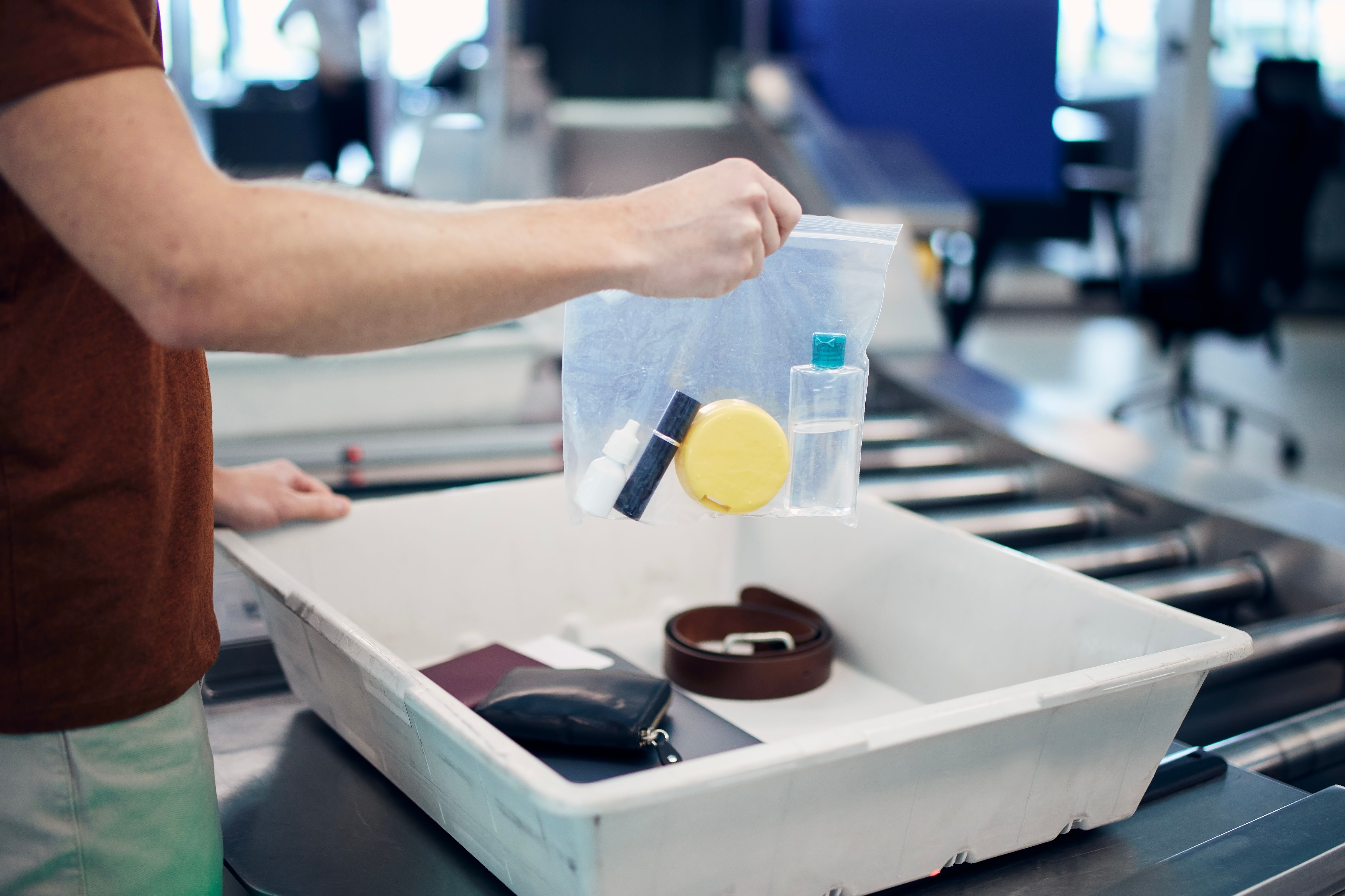 A passenger placing a zip bag filled with small liquid items into an airport security bin.