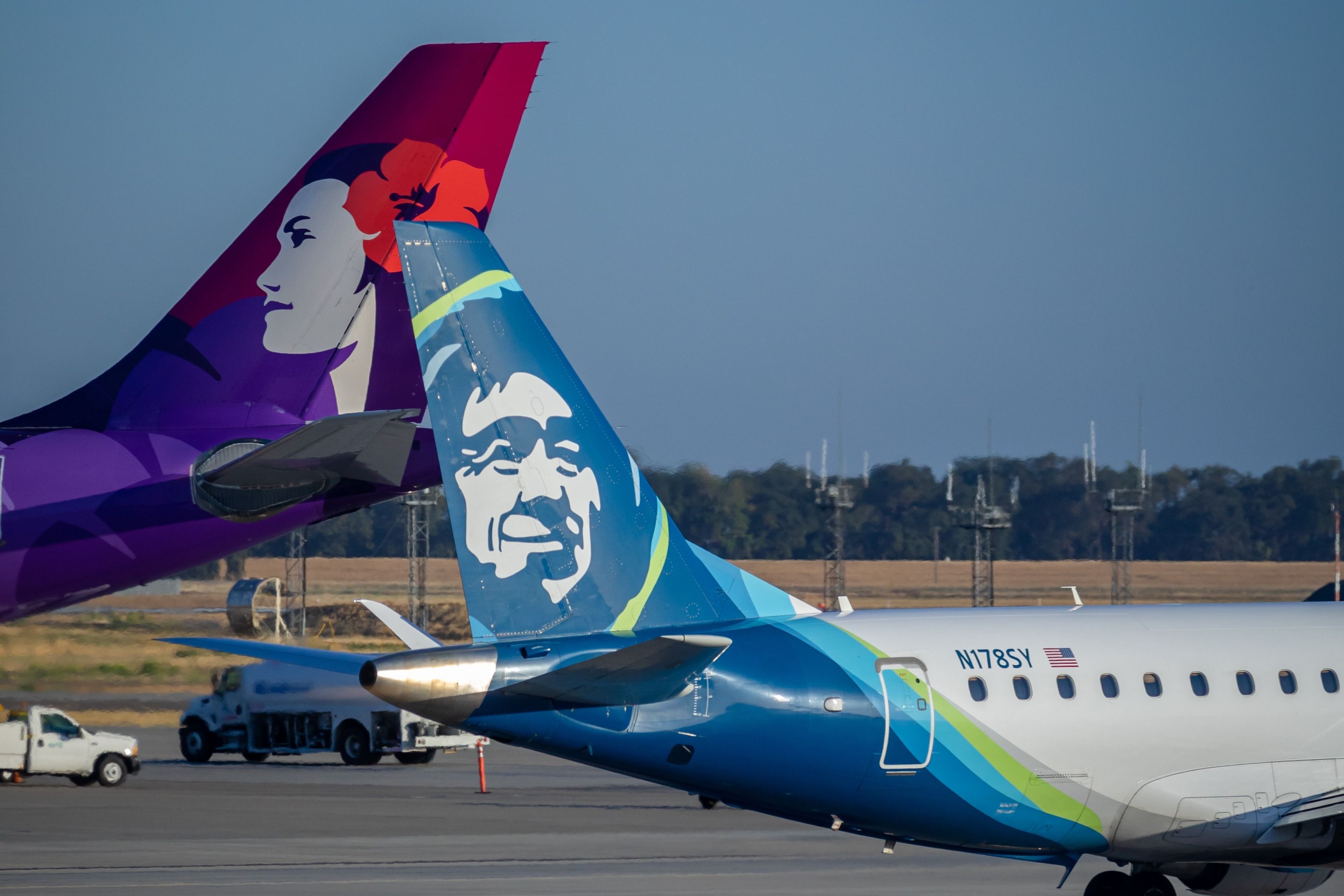 An Alaska Airlines Embraer E175 (Operated by SkyWest Airlines) tail and a Hawaiian Airlines Airbus A330 tail at Sacramento International Airport.