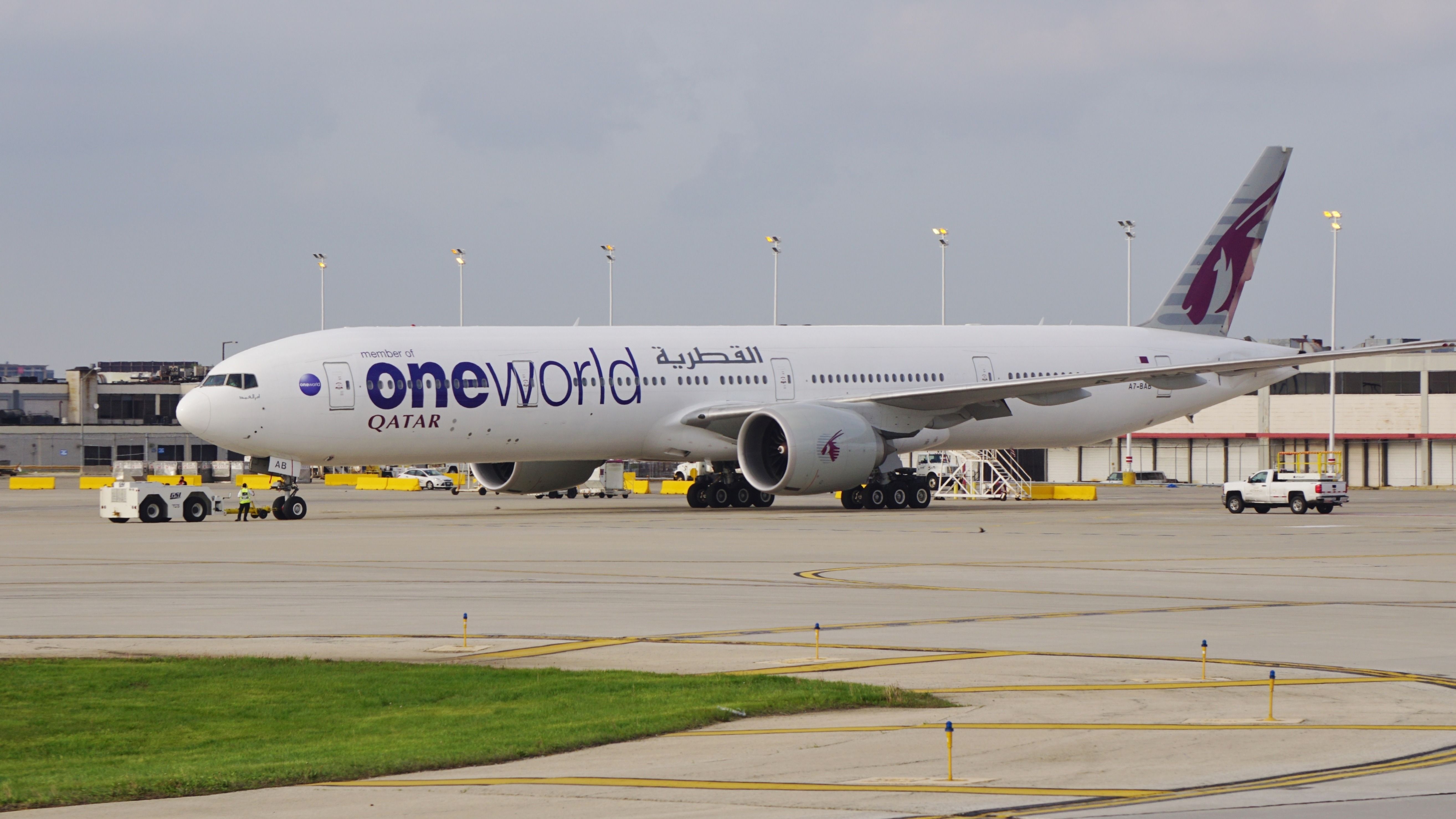 A Qatar Airways 777-300ER in OneWorld livery on an airport apron.