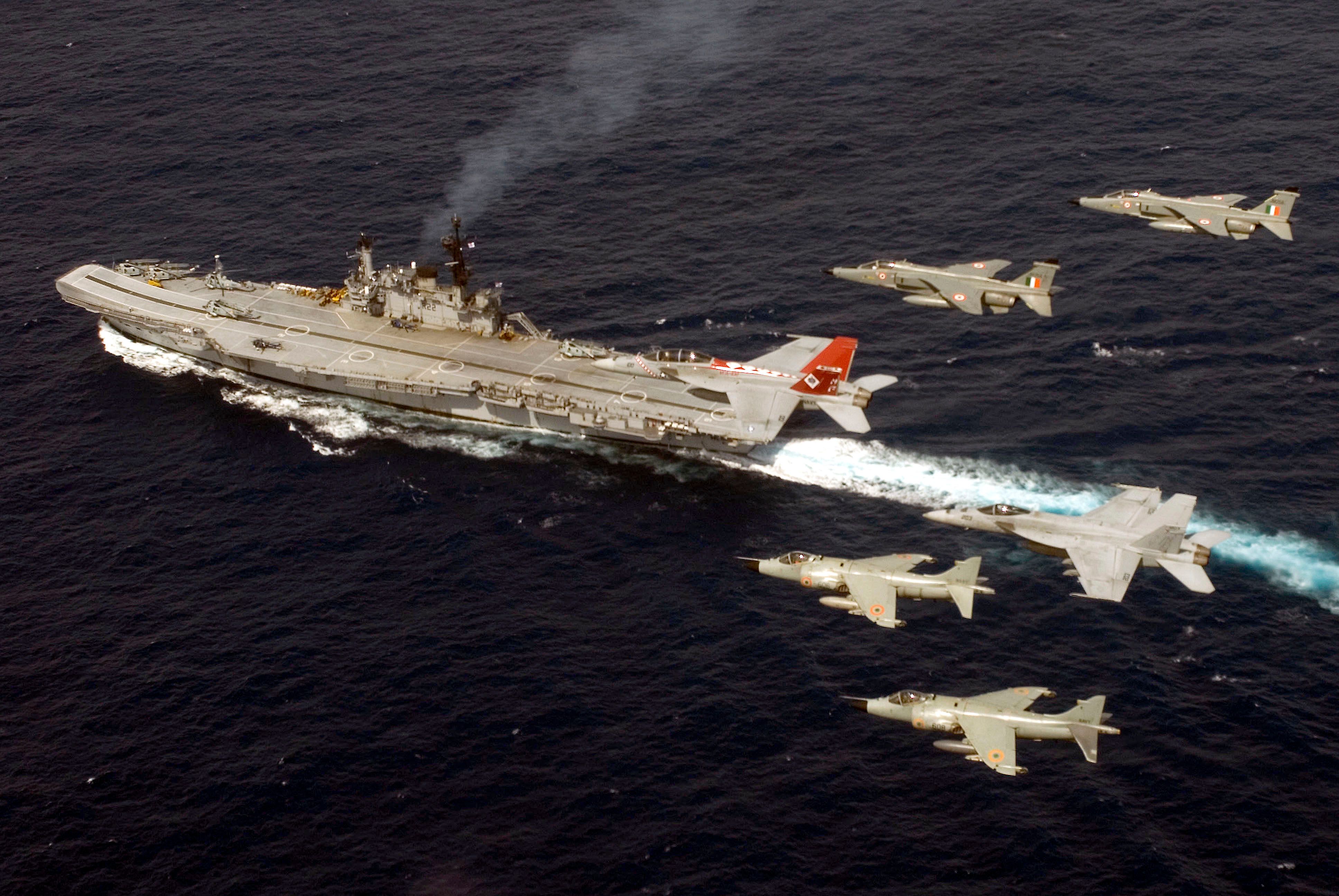 Several Indian Air Force SEPECAT Jaguar Attack fighters flying above an aircraft carrier.