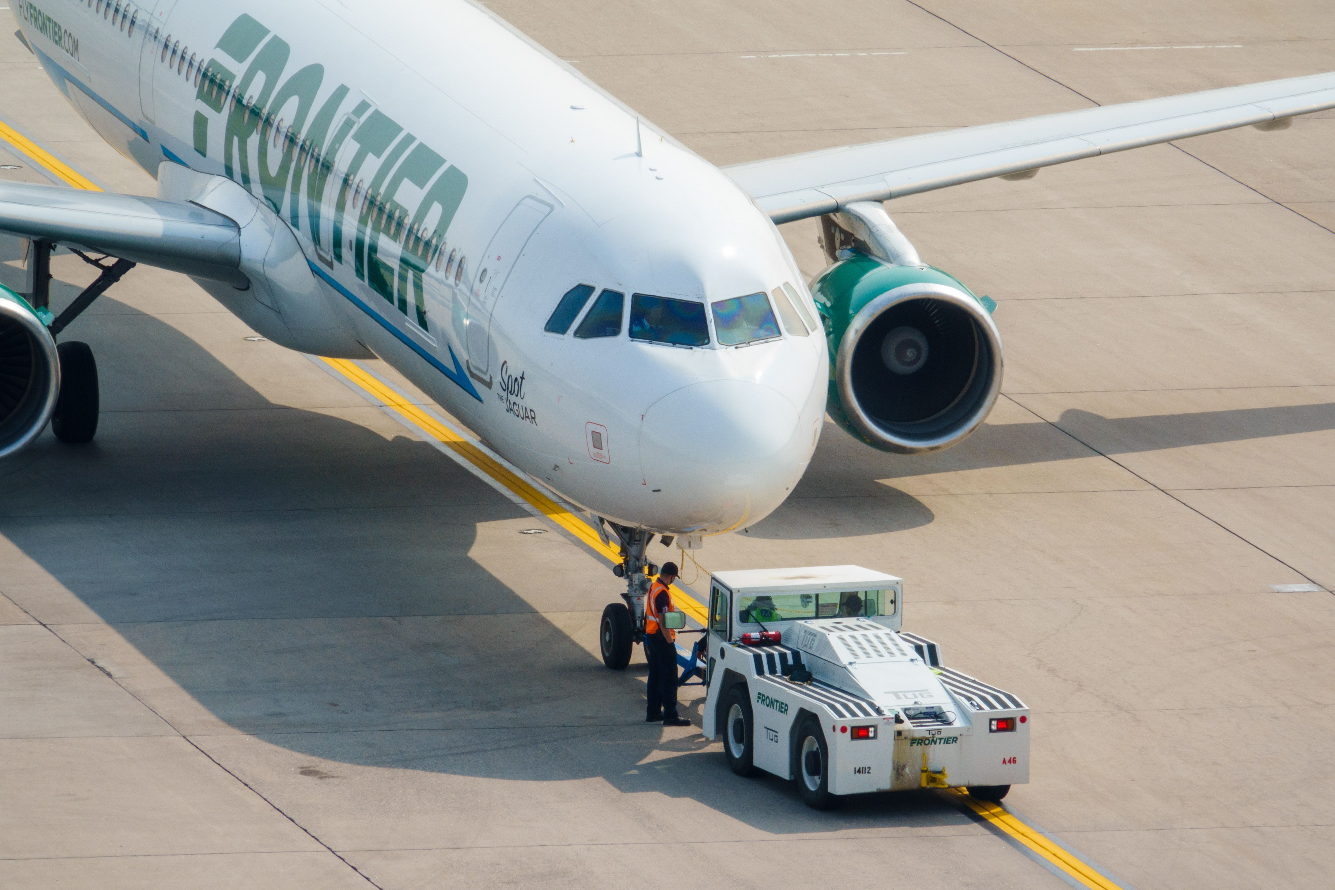 A Frontier Airlines plane being towed by a tug