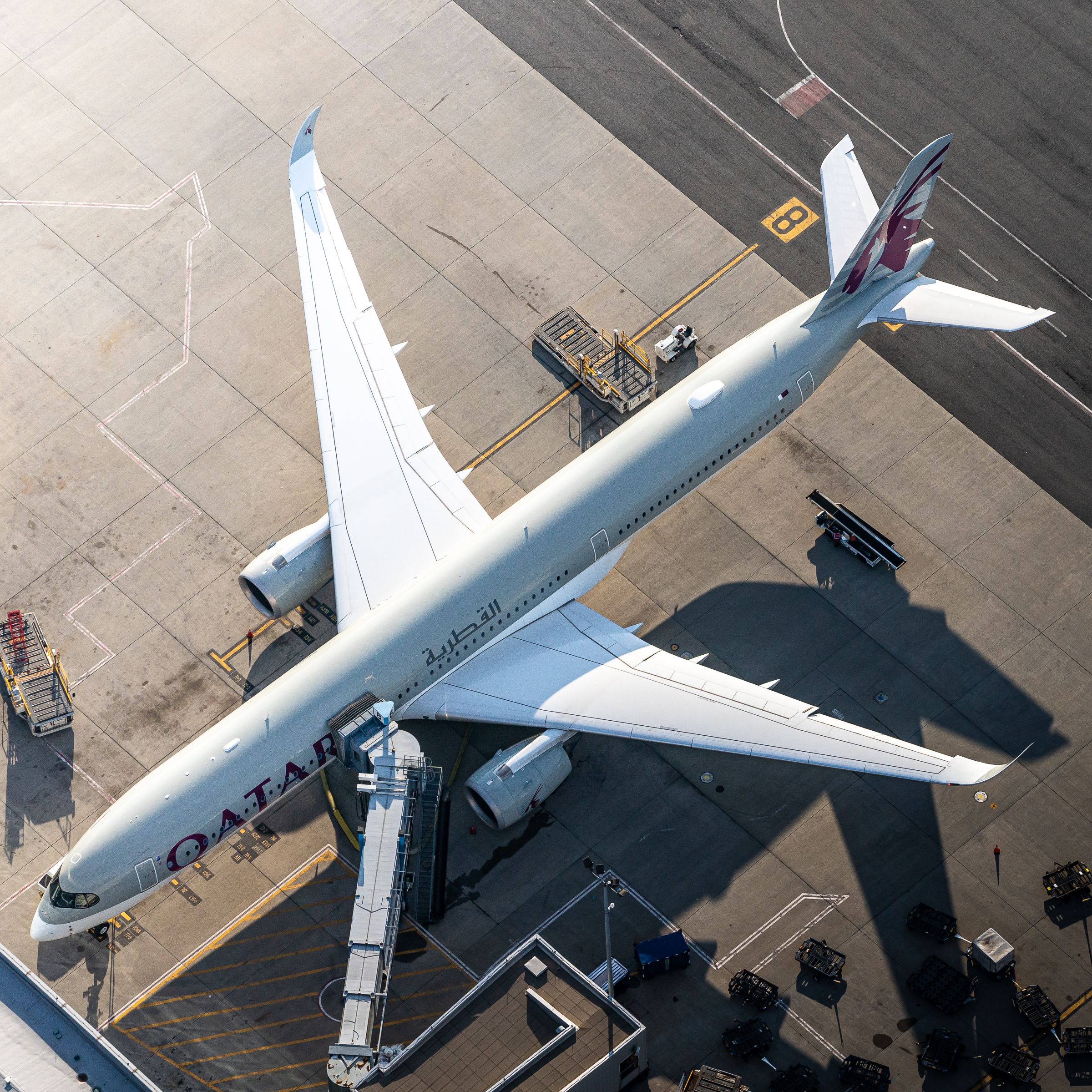 A Qatar Airways Airbus A350-1041 on an airport apron parked at a gate.