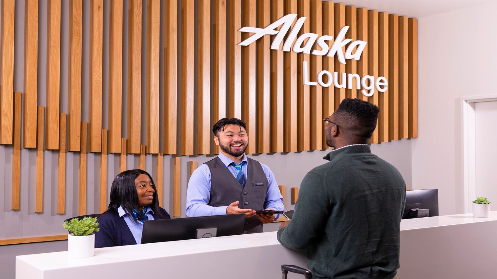 A traveler speaking with agents at an Alaska Airlines Lounge desk.