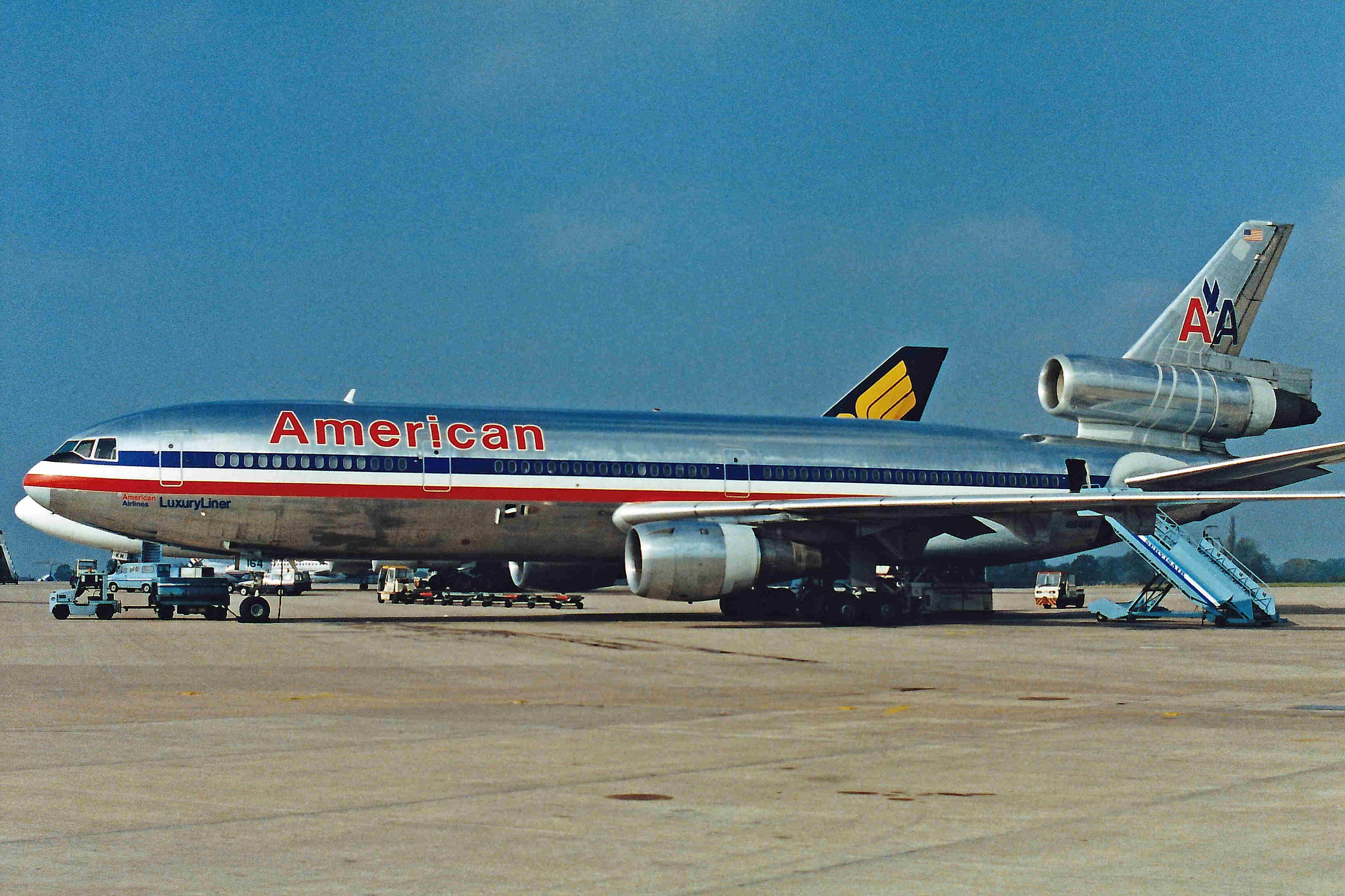 An American Airlines DC-10  on an airport apron parked next to a Singapore Airlines aircraft.