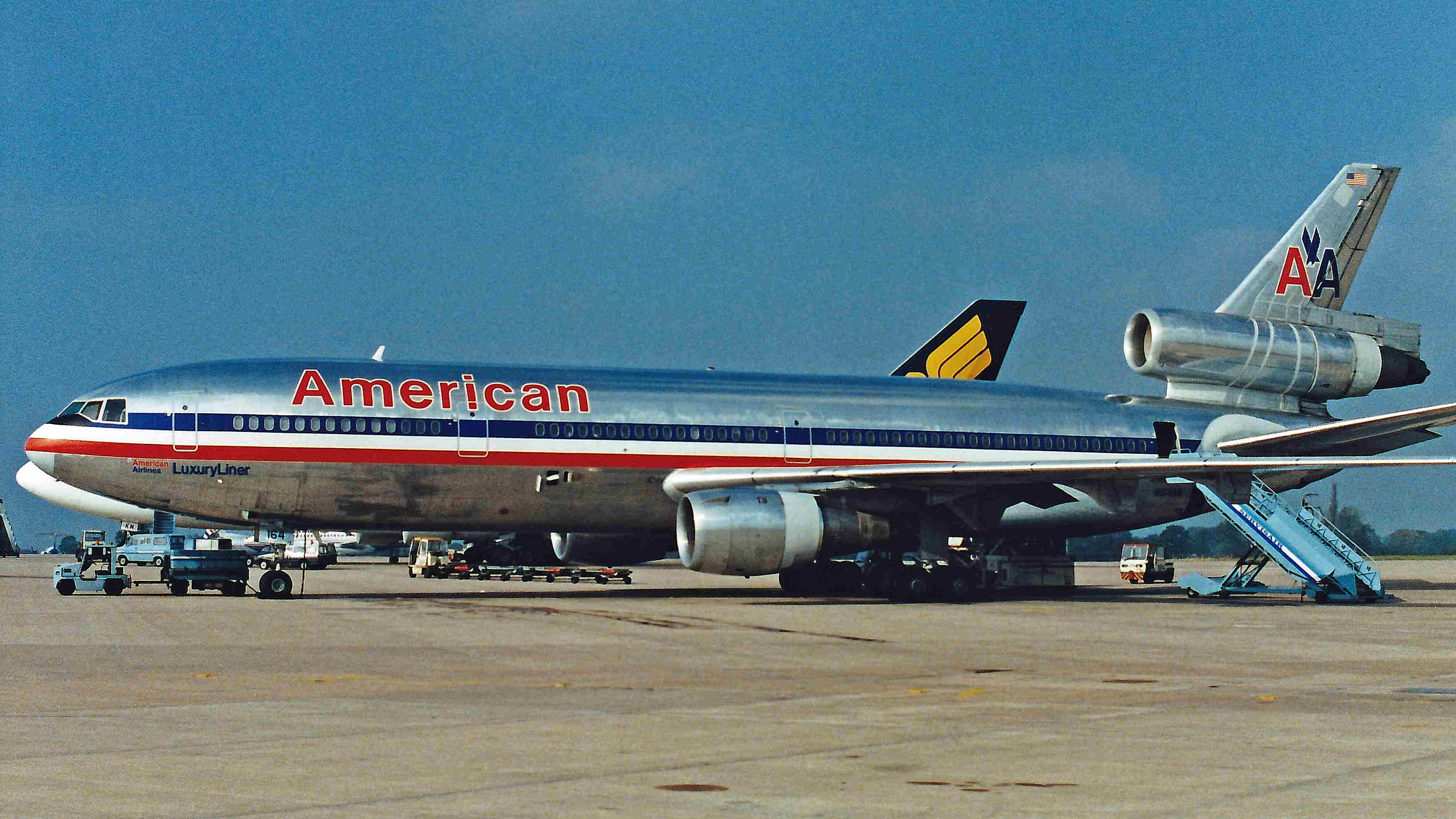 An American Airlines DC-10  on an airport apron parked next to a Singapore Airlines aircraft.