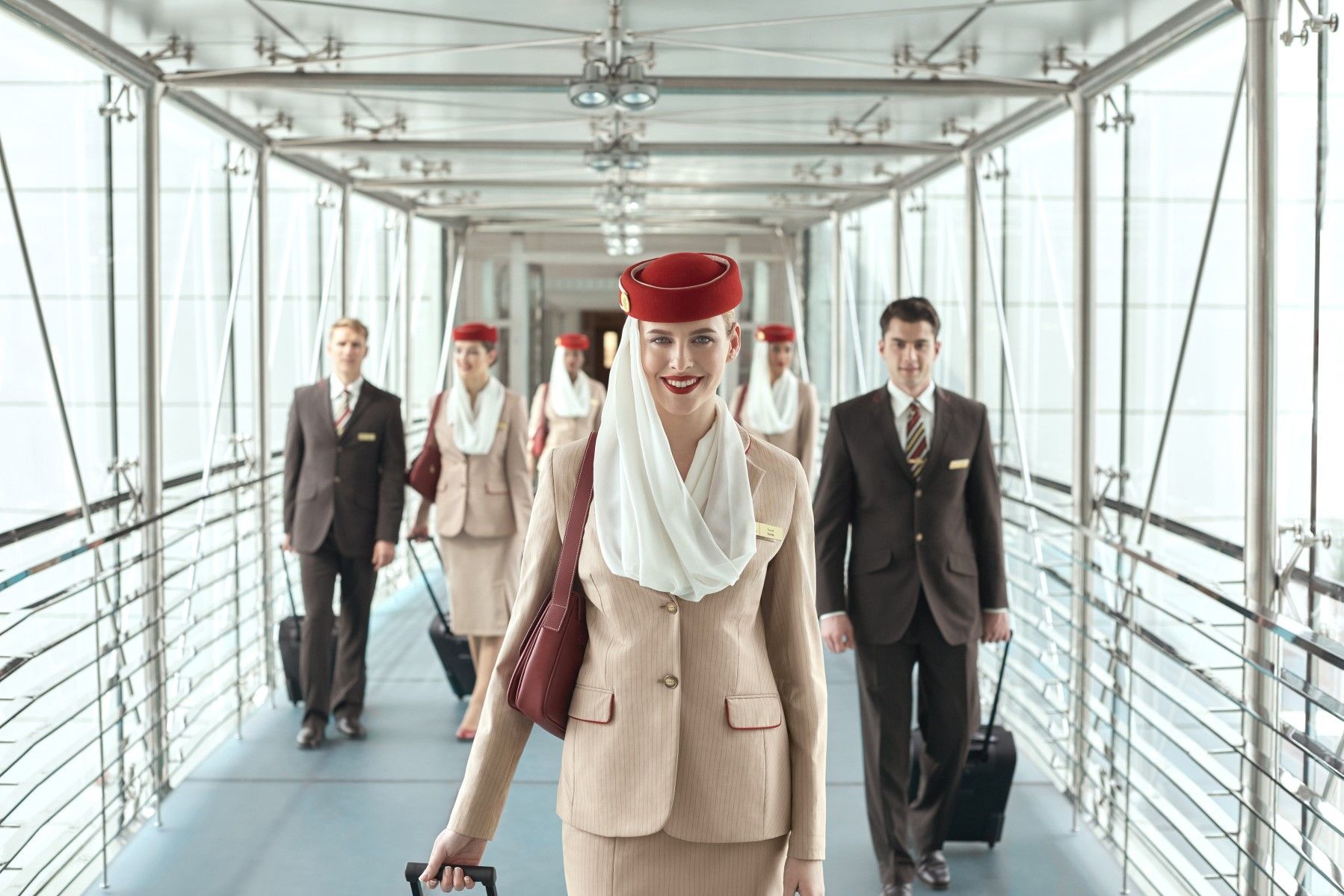 Several Emirates crew members walking on a jet bridge.