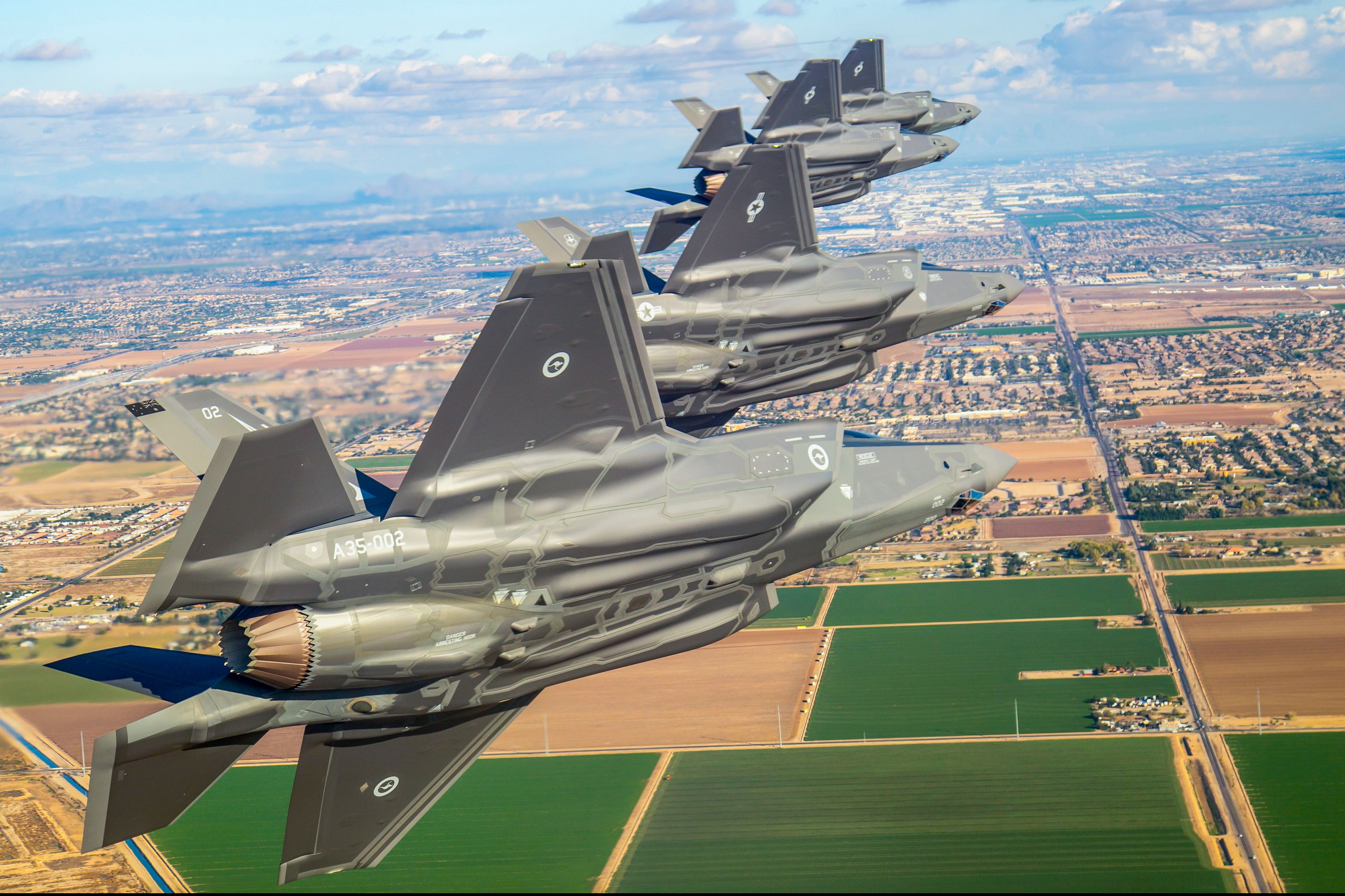 A First Royal Australian Air Force F-35A Lightning II flying alongside multiple USAF F-35s.