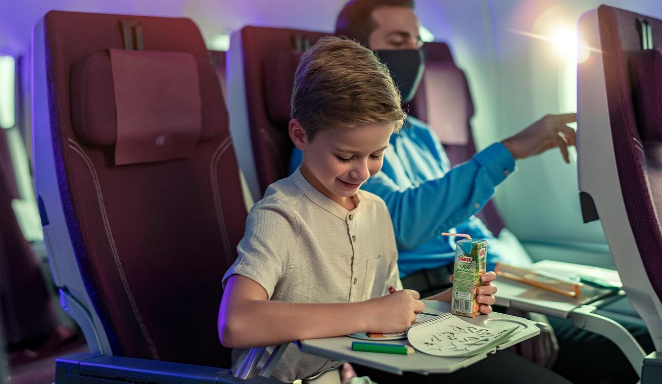 A child and father sitting side by side in the Qatar Airways economy class cabin.