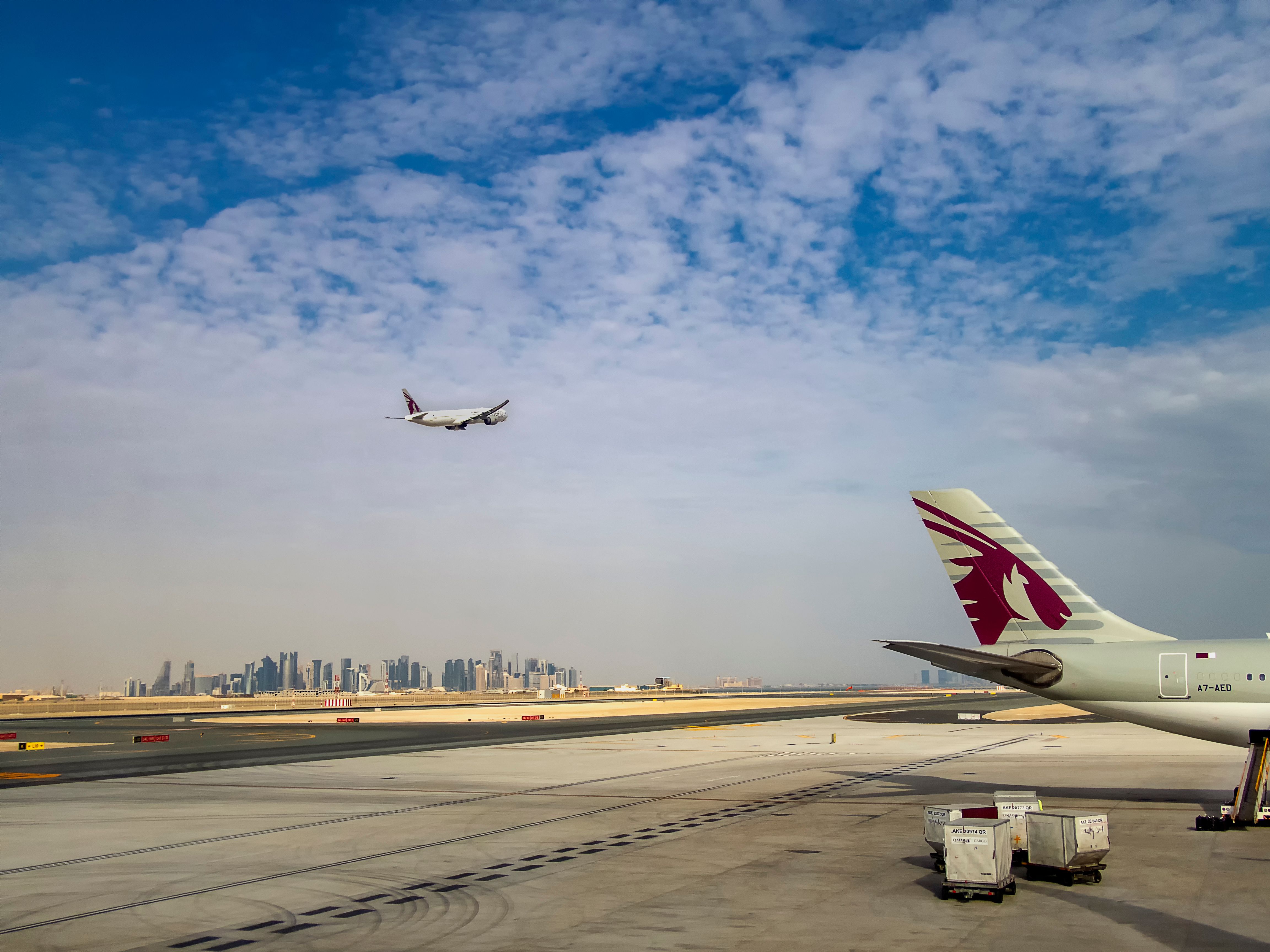 Multiple Qatar Airways aircraft in the sky and on the apron at Doha's Hamad International Airport.