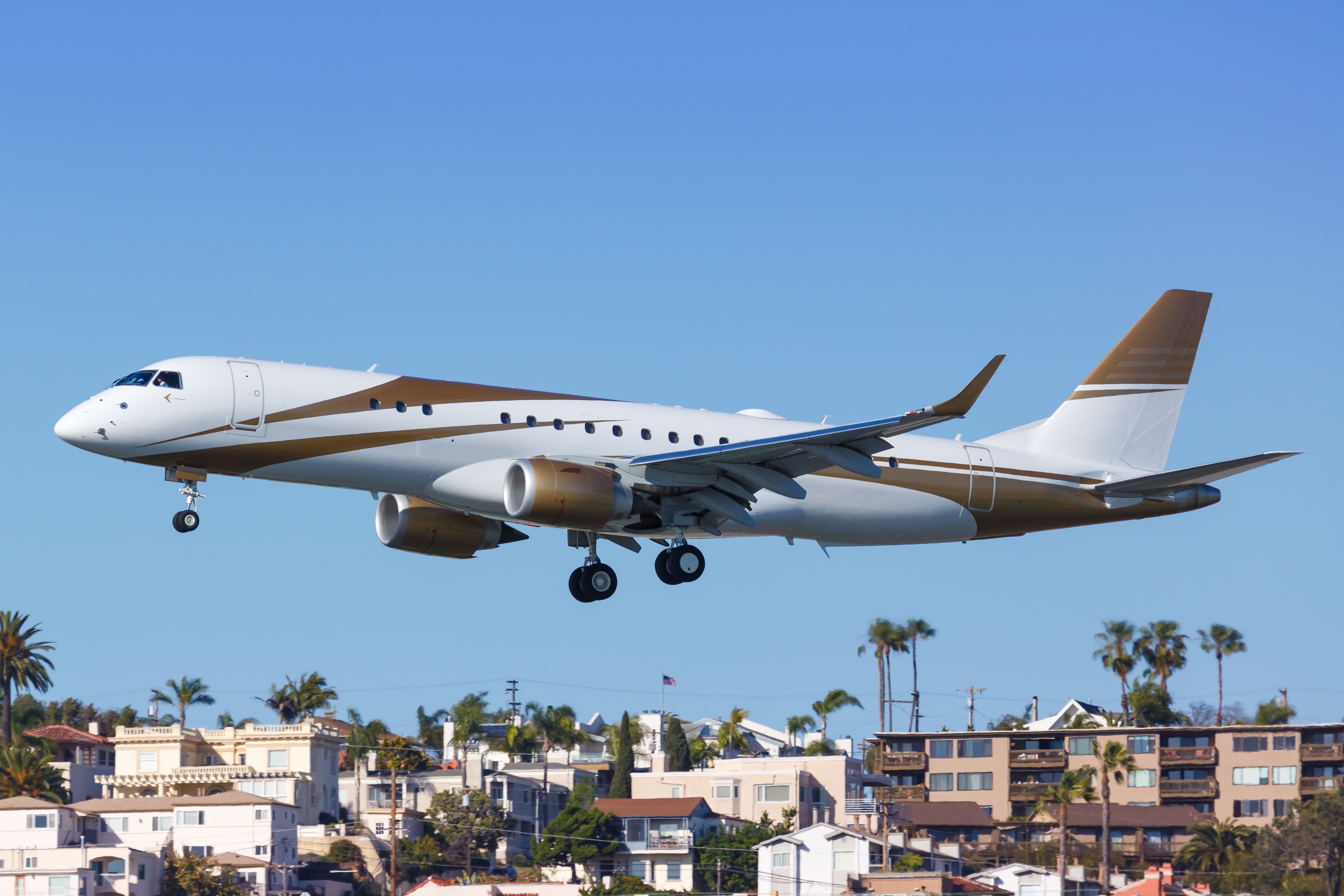 An Embraer Lineage 1000E flying low to the ground with houses in the background.