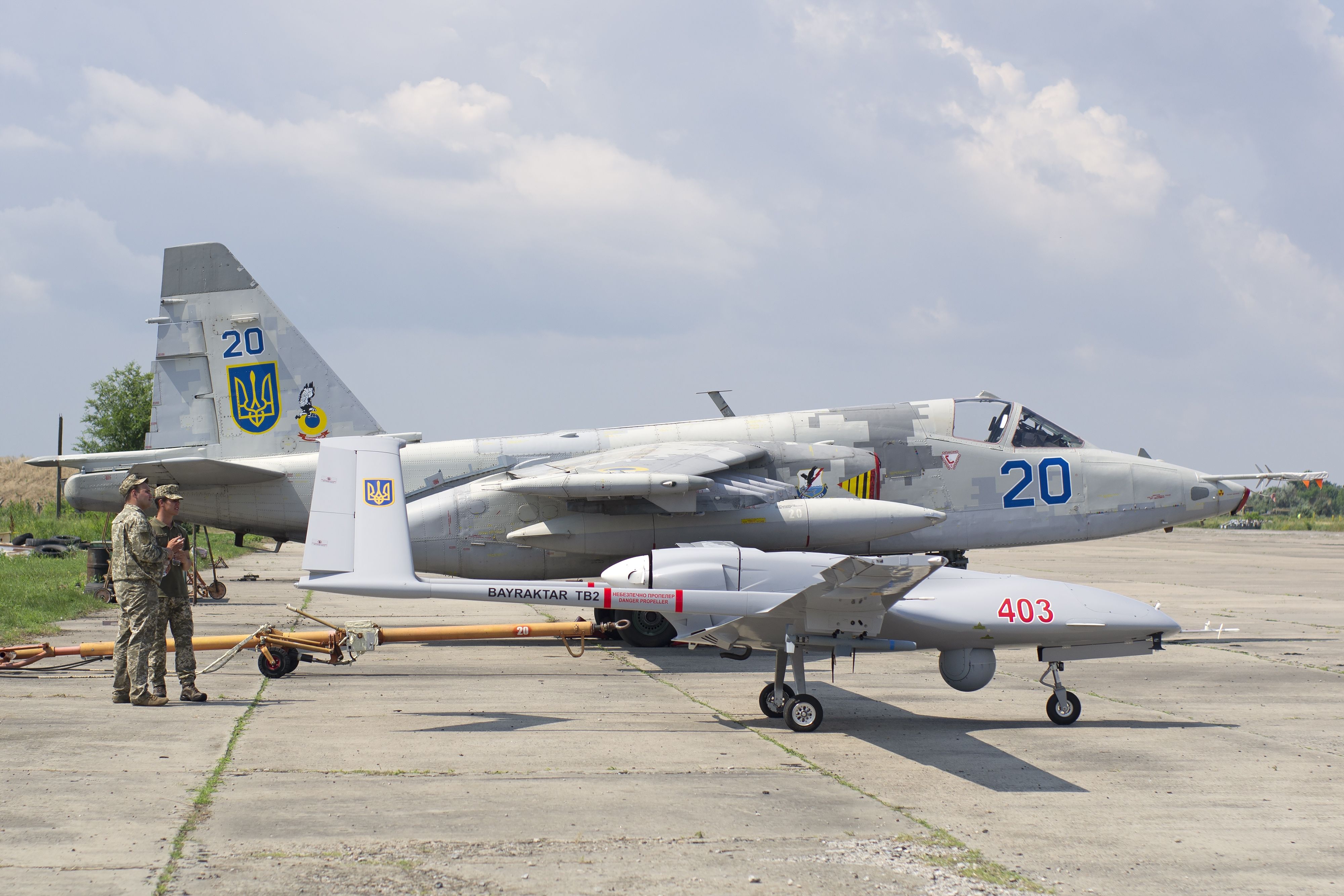 A Ukrainian Sukhoi Su-25 parked on a military airfield next to a drone.