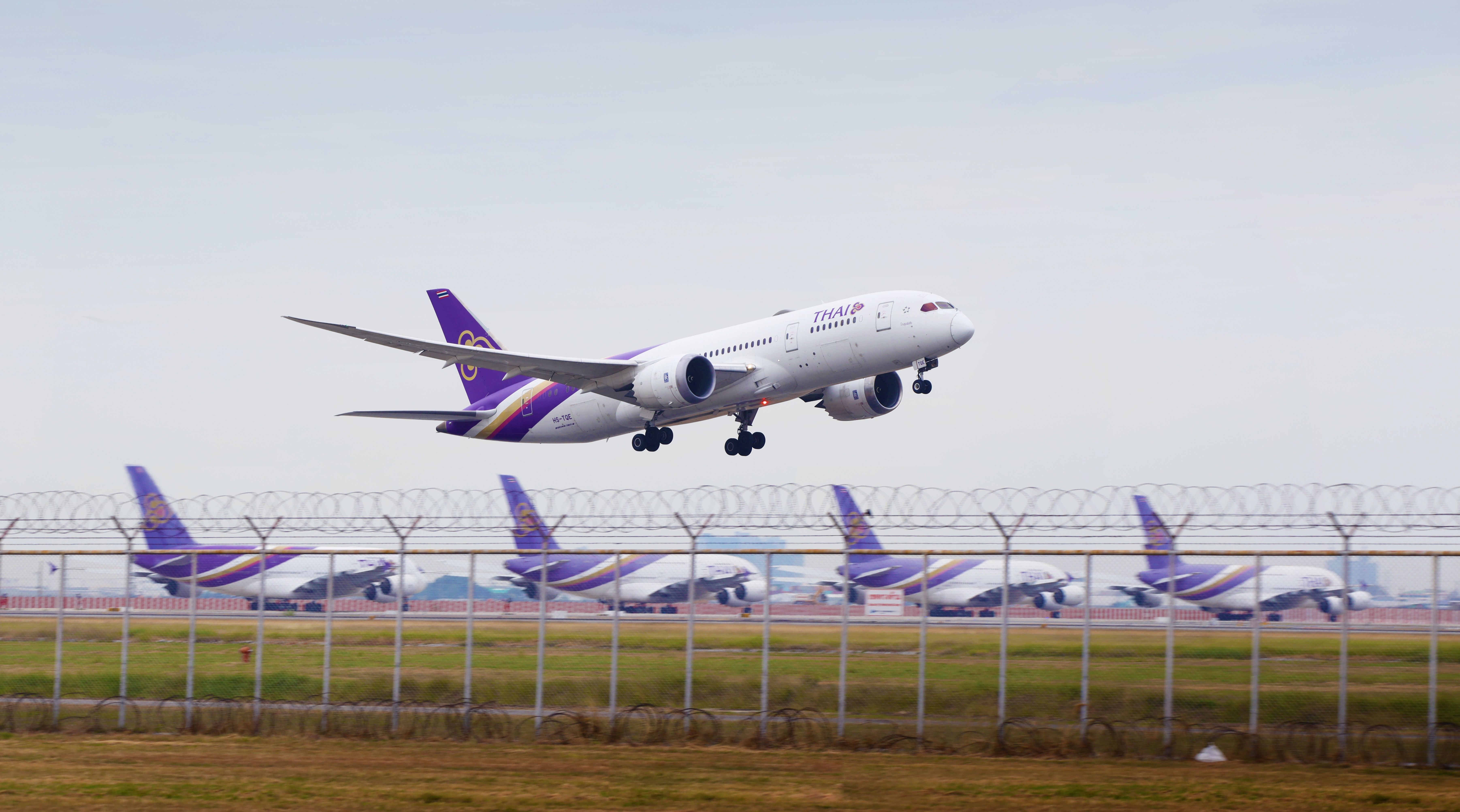 A Thai Airways Boeing 787 taking off from Bangkok Suvarnabhumi International Airport in front of parked Airbus A380 superjumbos