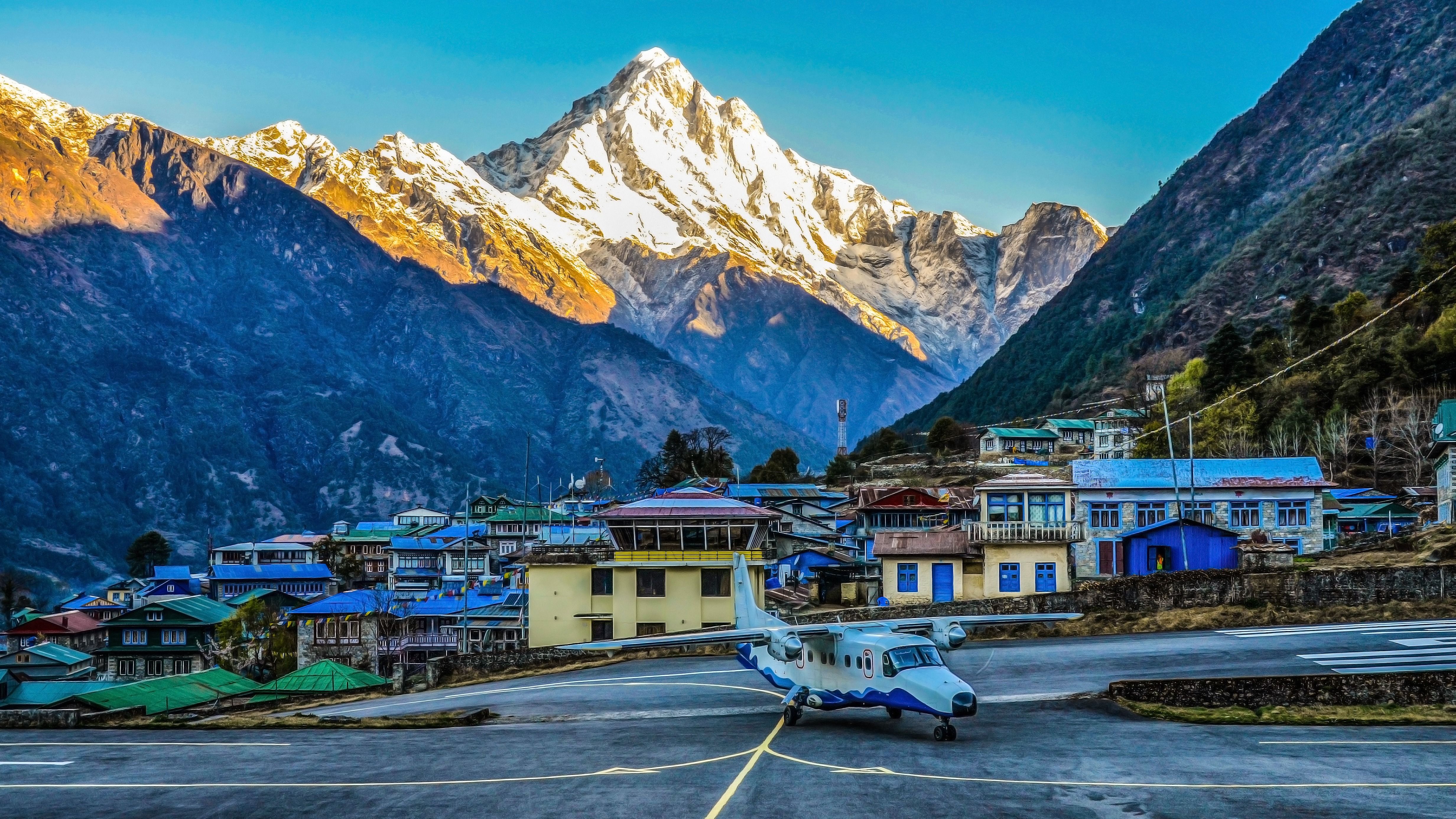 An aircraft on the apron at Lukla airport with a town and mountains in the background.