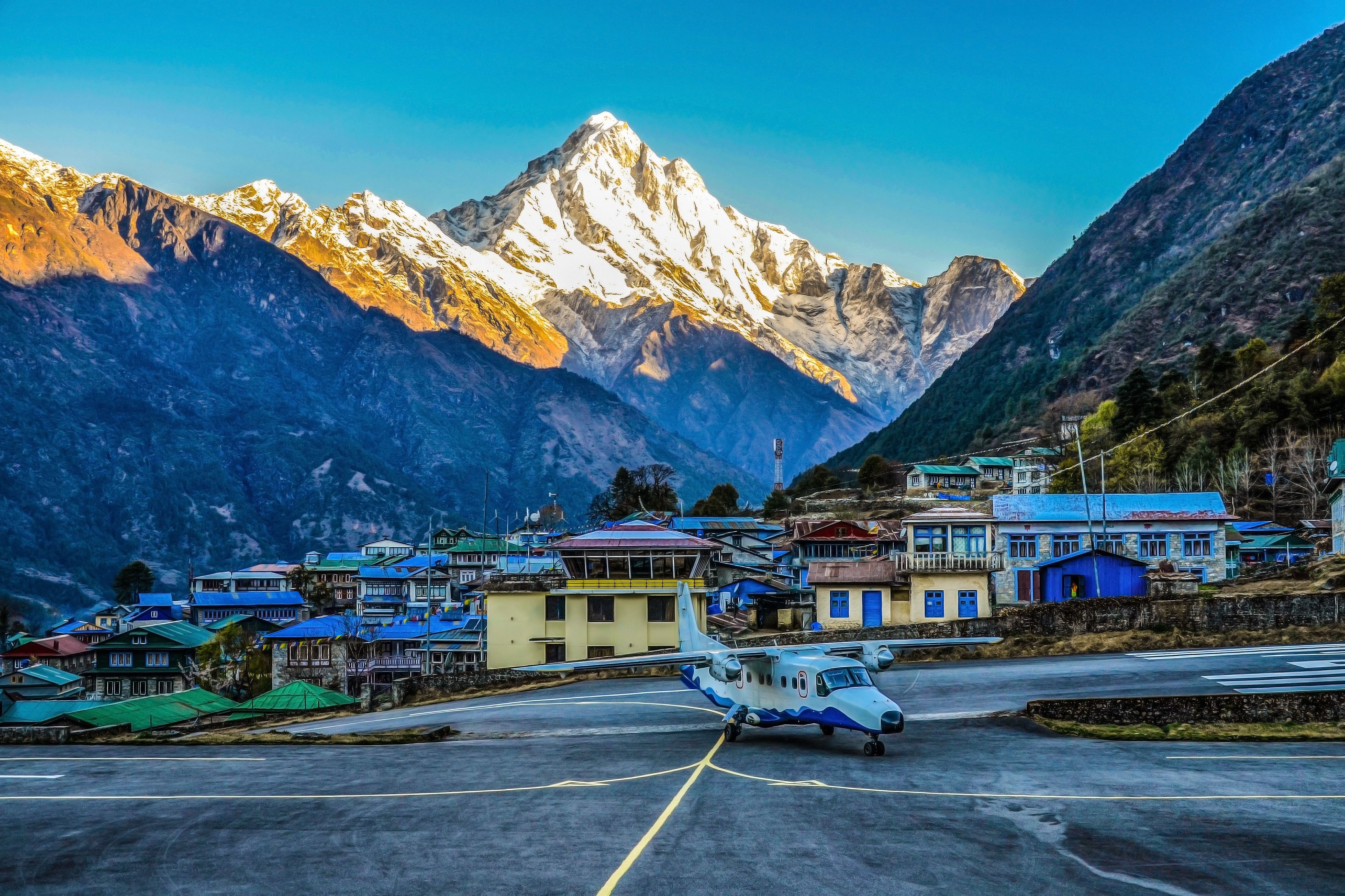 An aircraft on the apron at Lukla airport with a town and mountains in the background.