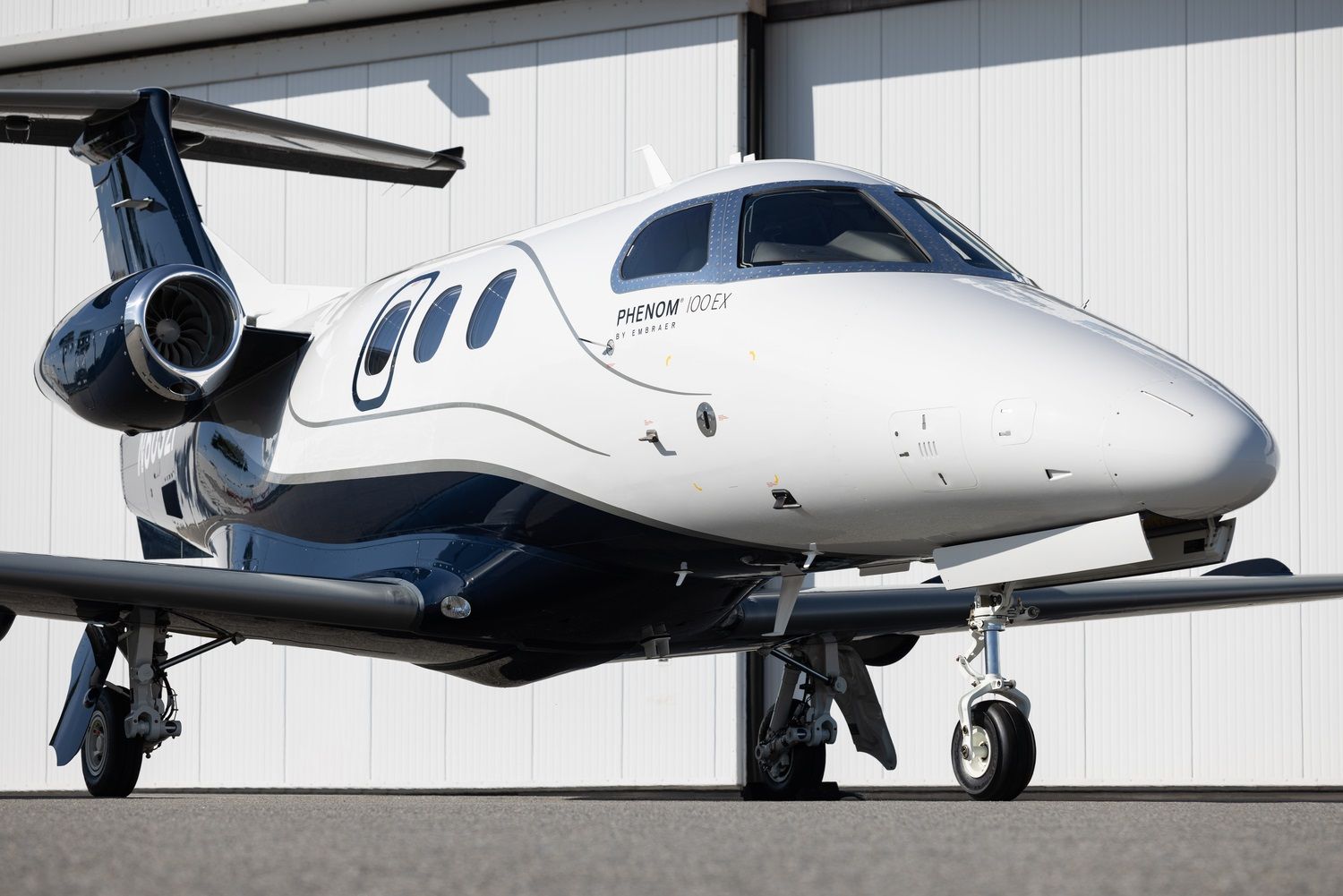 An Embraer Phenom 100 parked in front of a hangar.