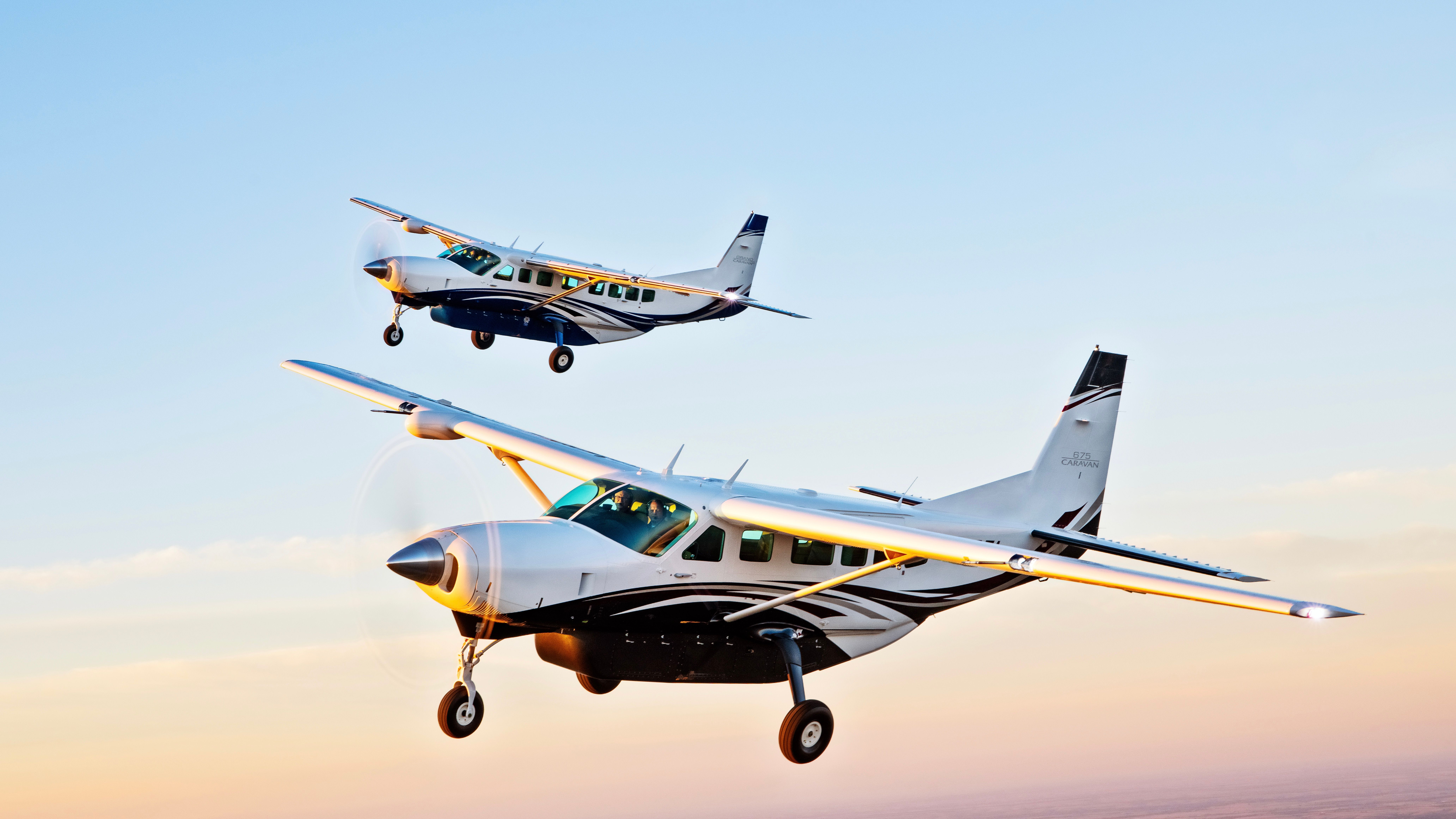 Two Cessna Caravan 208s flying in the sky in formation.