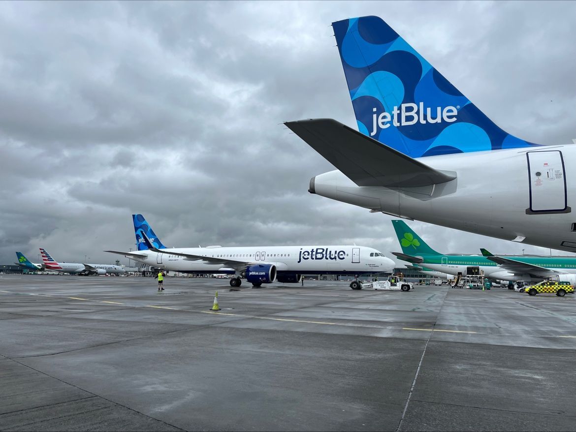 Two jetBlue aircraft on an airport apron next to Aer Lingus aircraft.