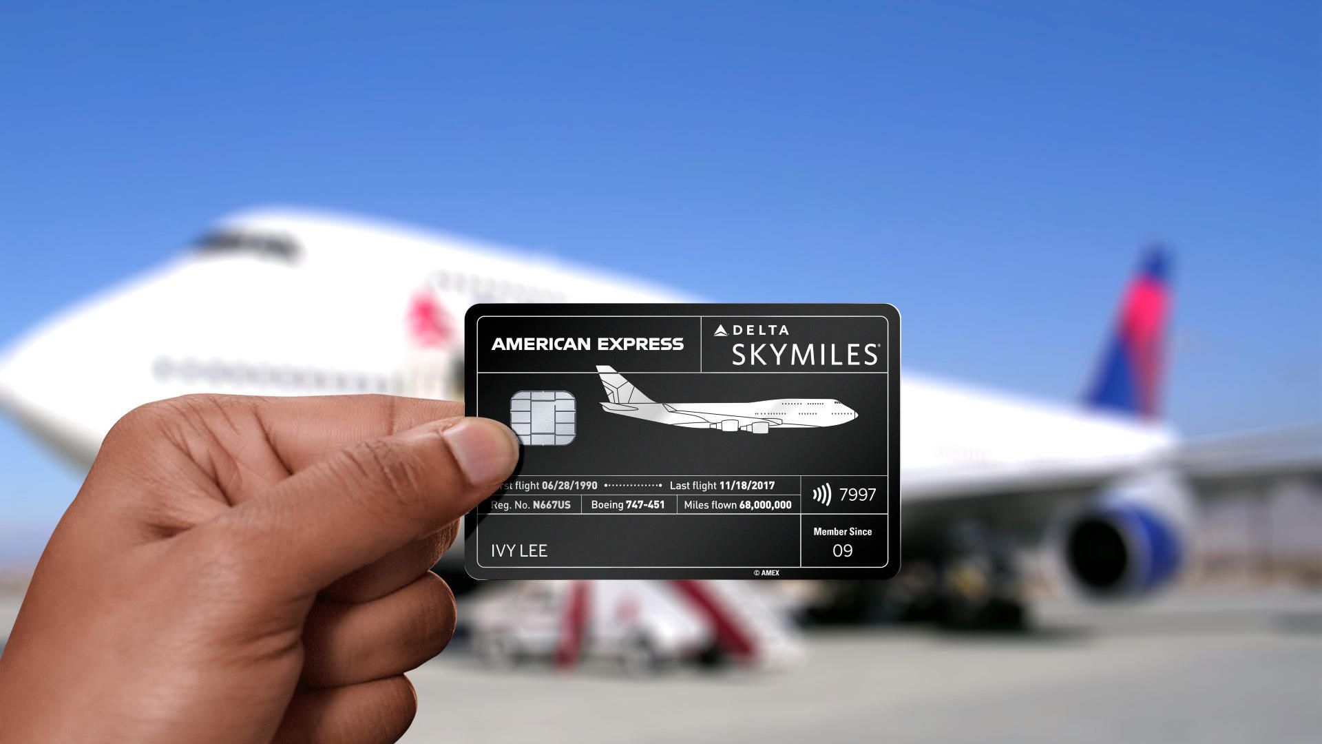 Someone holding a Delta Skymiles American Express card in front of a Delta Air Lines Boeing 747.