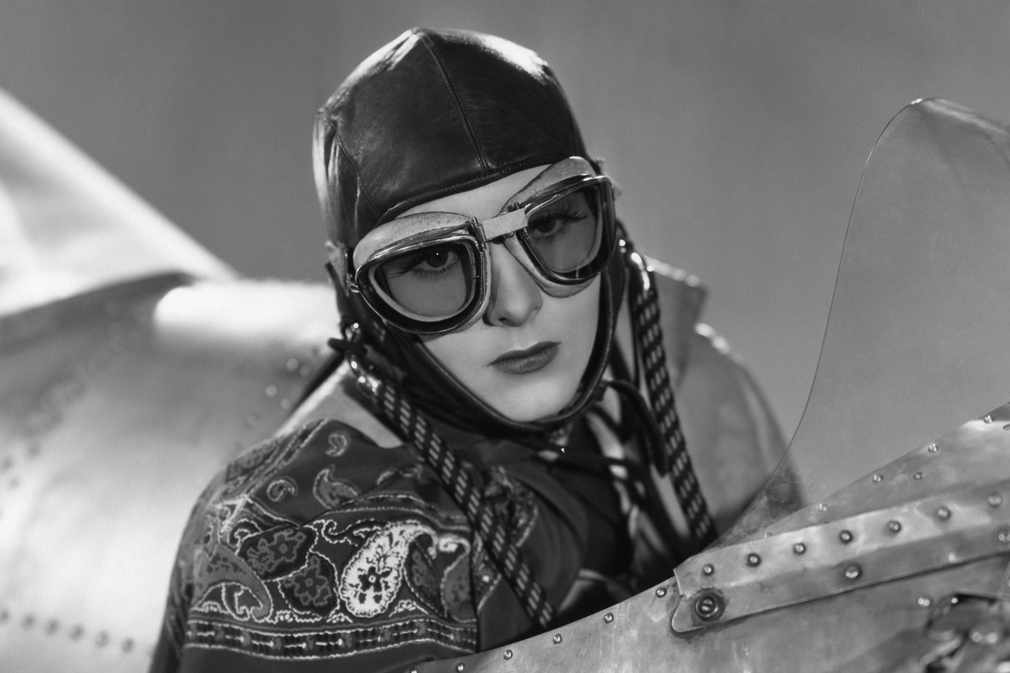 A woman wearing goggles in the cockpit of an old aircraft.