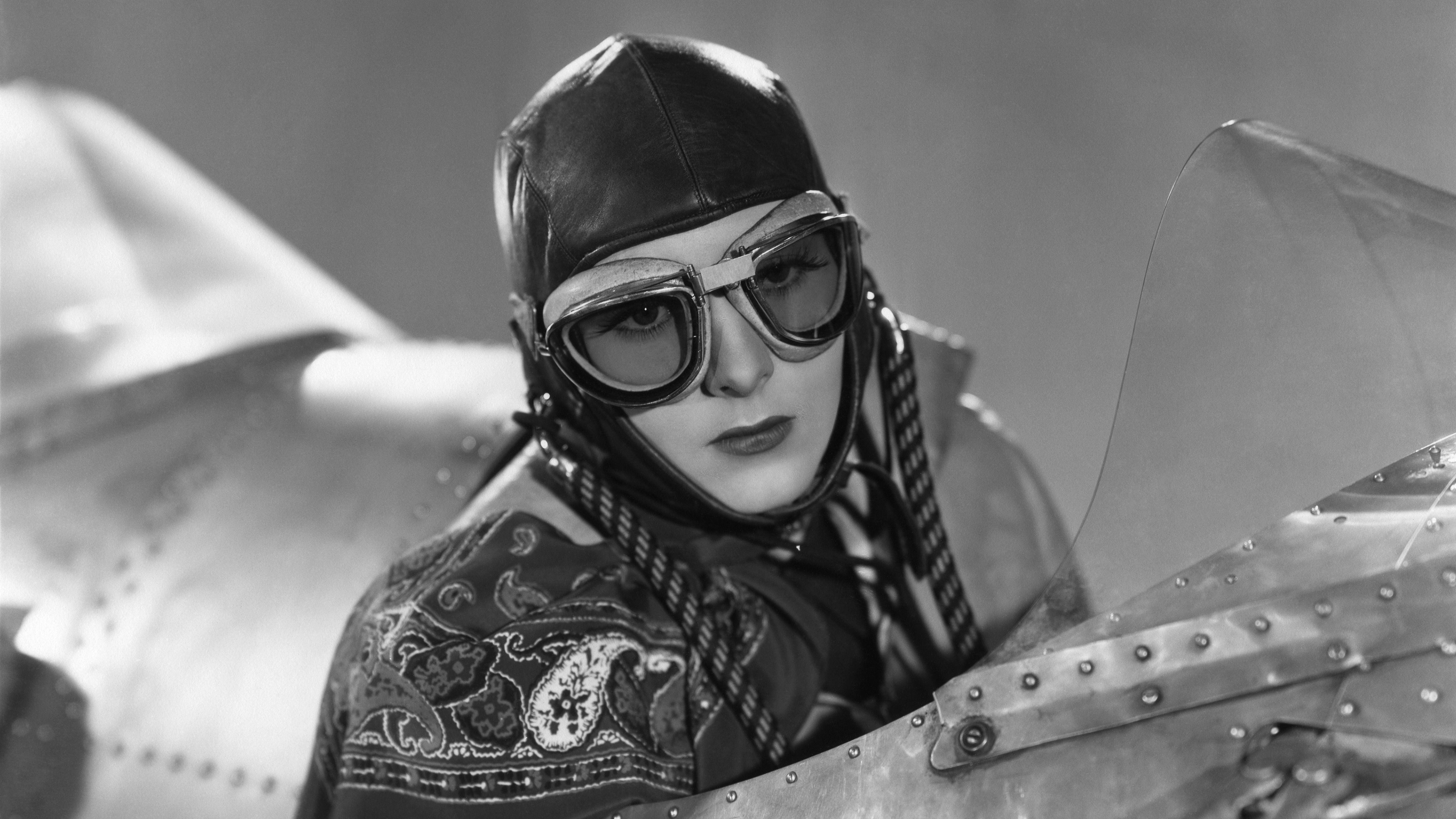 A woman wearing goggles in the cockpit of an old aircraft.