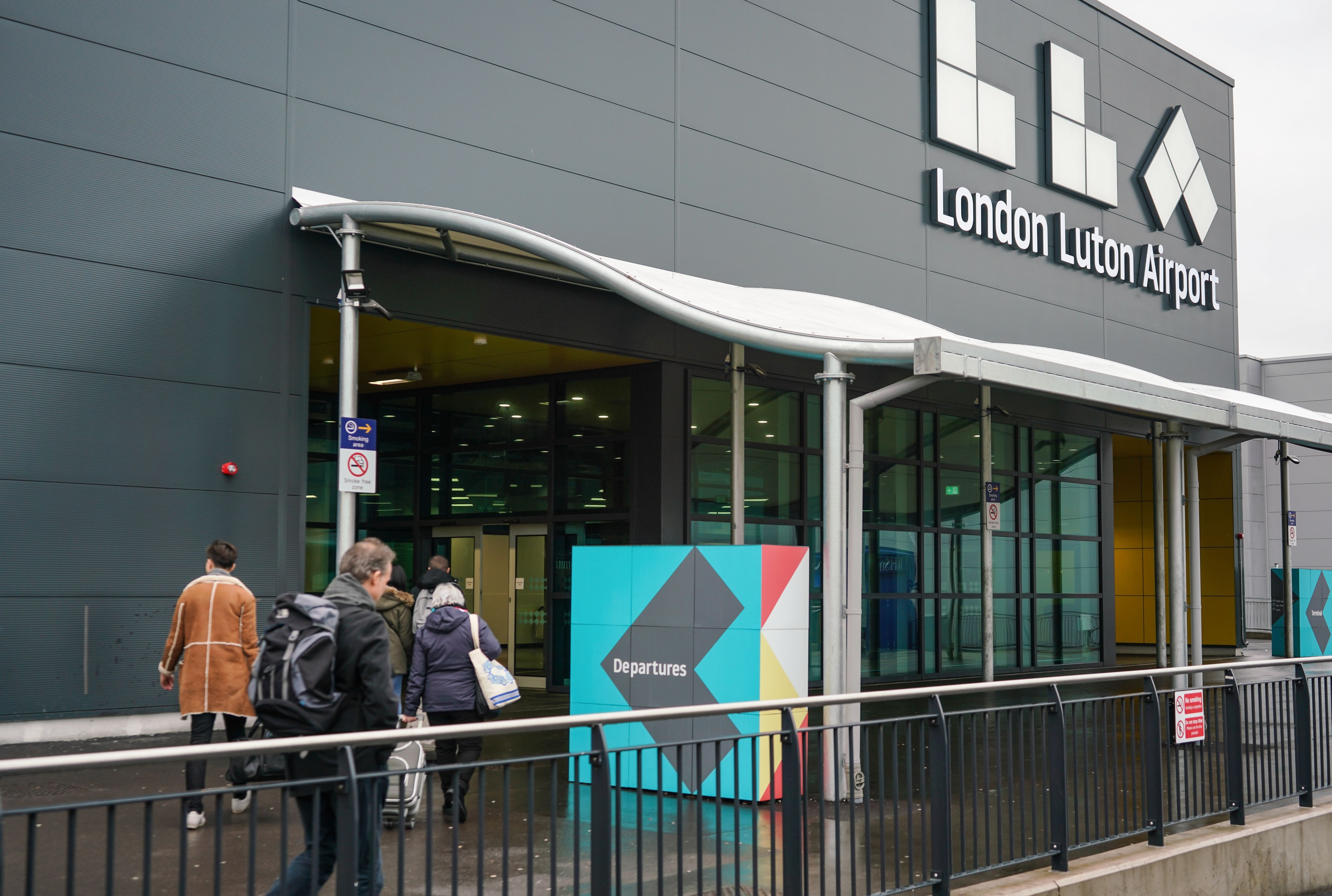 Three passengers outside the entrance to the London Luton Airport terminal.