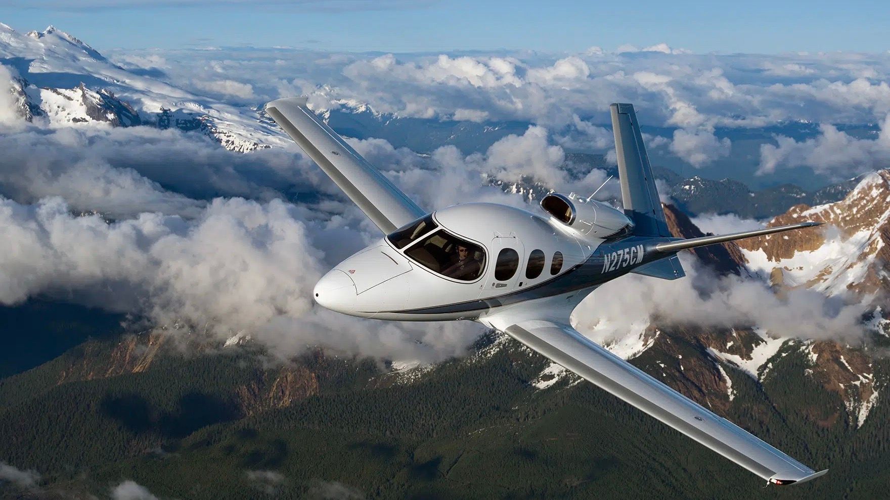 A Cirrus G2+ Vision Jet flying over mountainous terrain.