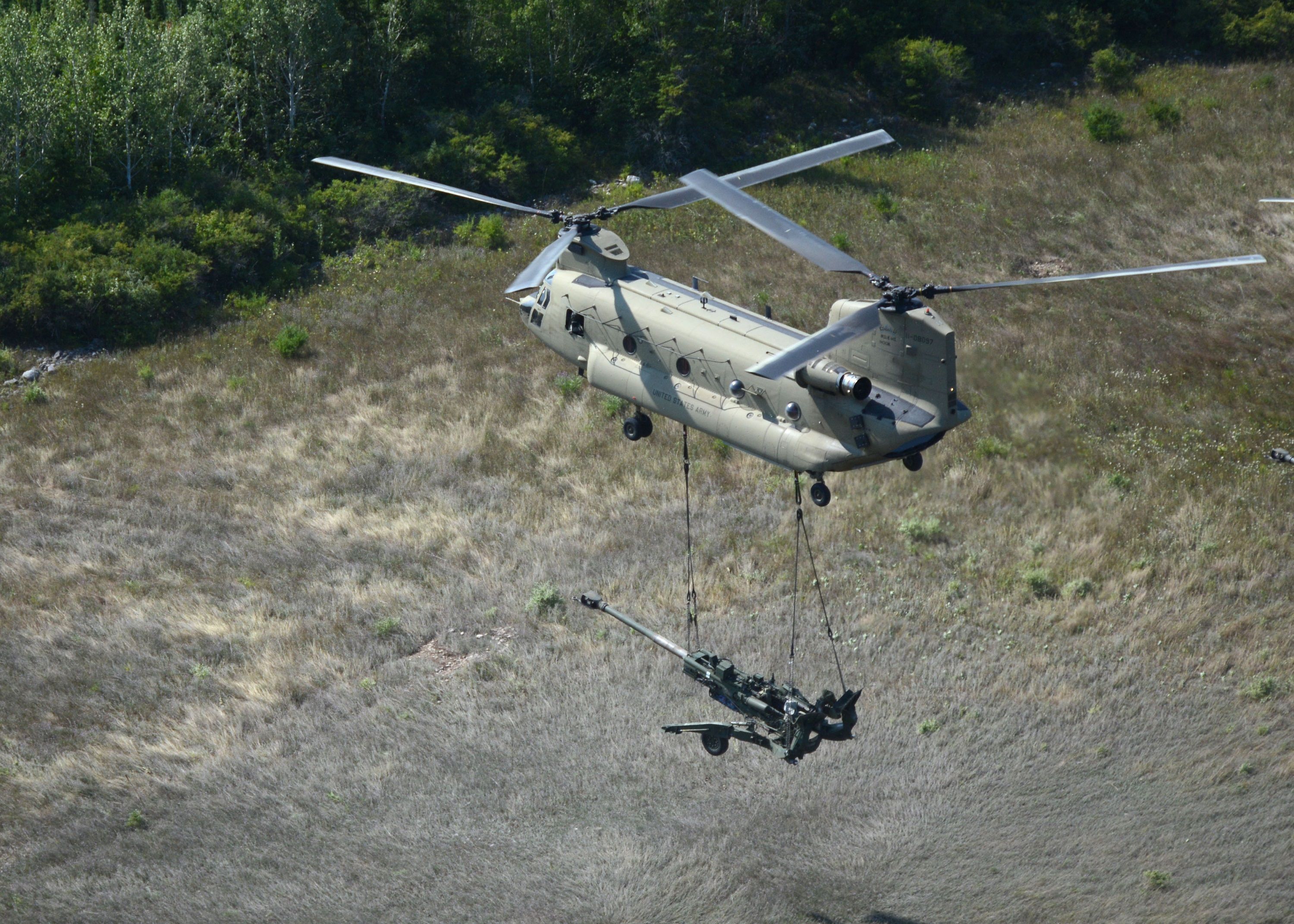 A US Army Boeing CH-47F Chinook carrying a massive cannon.