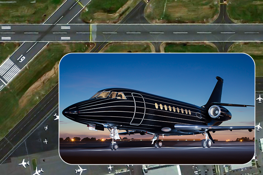 A black business jet with white stripes on an airport apron, with an aerial view of an airport in the background.