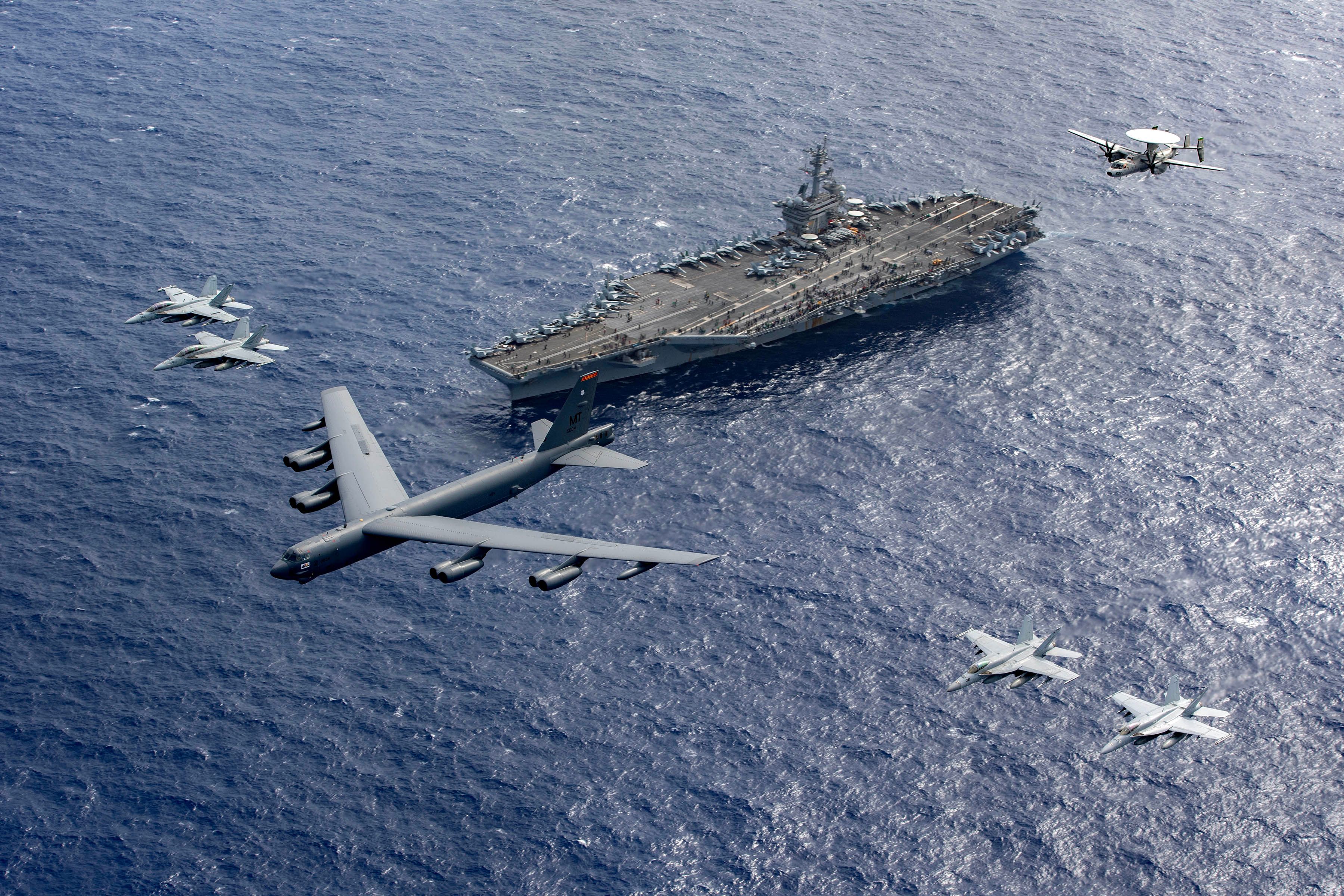 A Boeing B-52 Stratofortress being escorted by F-18 Super Hornets and an E-2 Hawkeye.