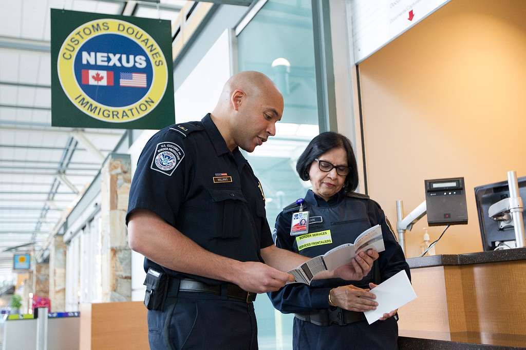 Two security officers looking at passports standing near a NEXUS customs and immigration sign.