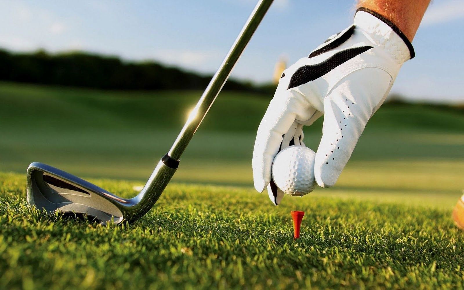 golfball on a tee with golf club and golfer's hand