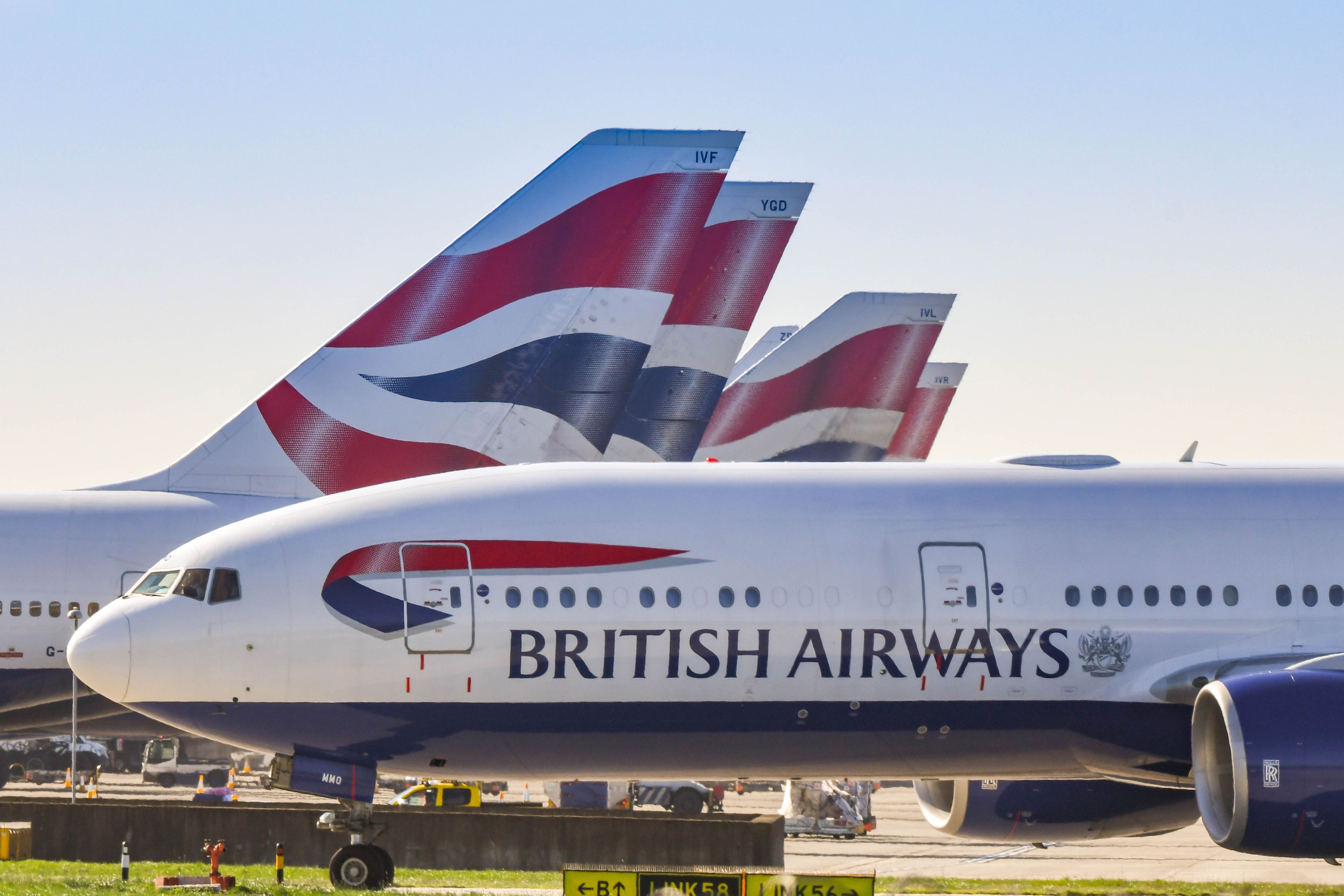 Boeing 777 long haul airliner operated by British Airways taxiing for take off at London Heathrow Airport past tail fins of the company's other aircraft.