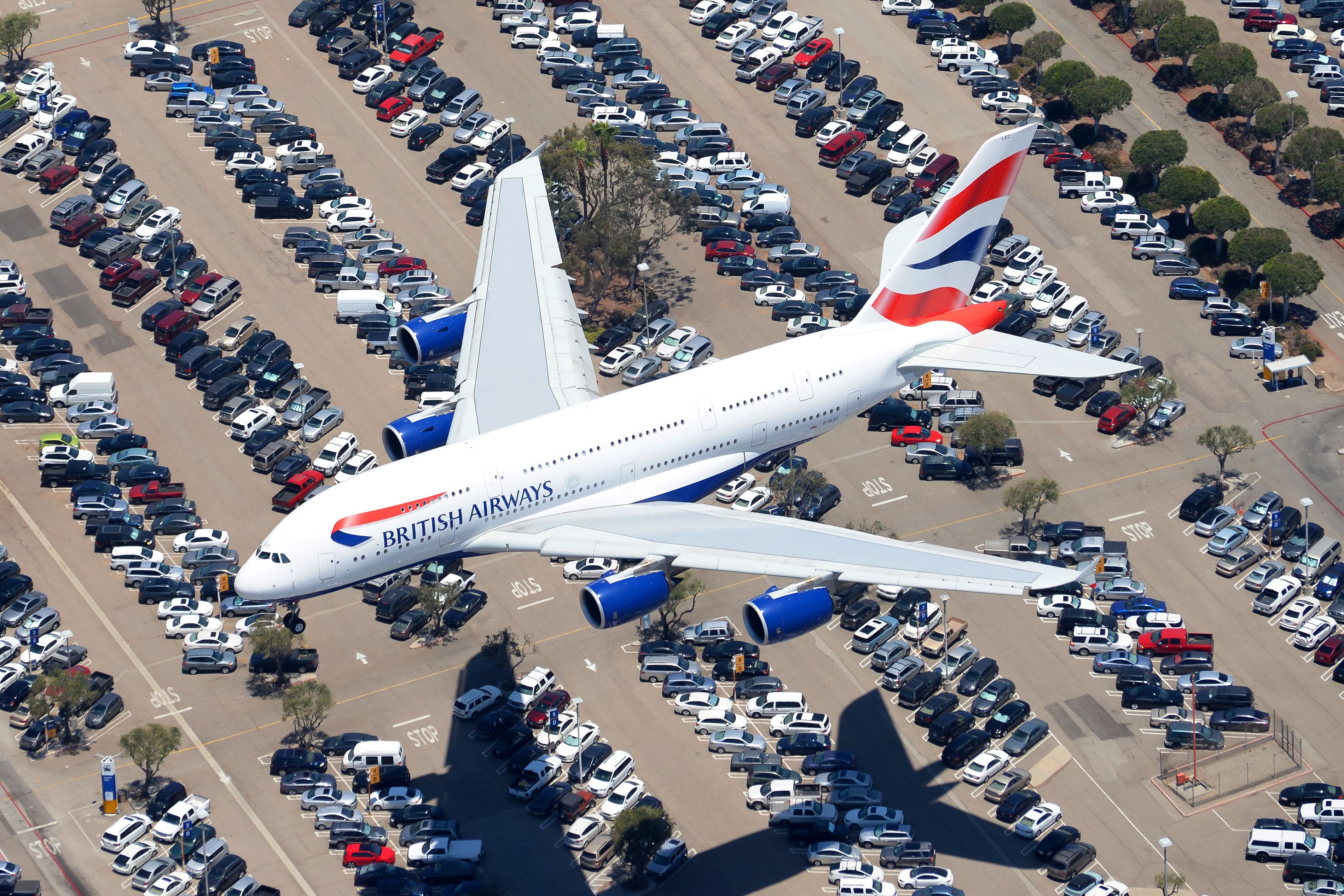 A British Airways Airbus A380 flying over parked cars