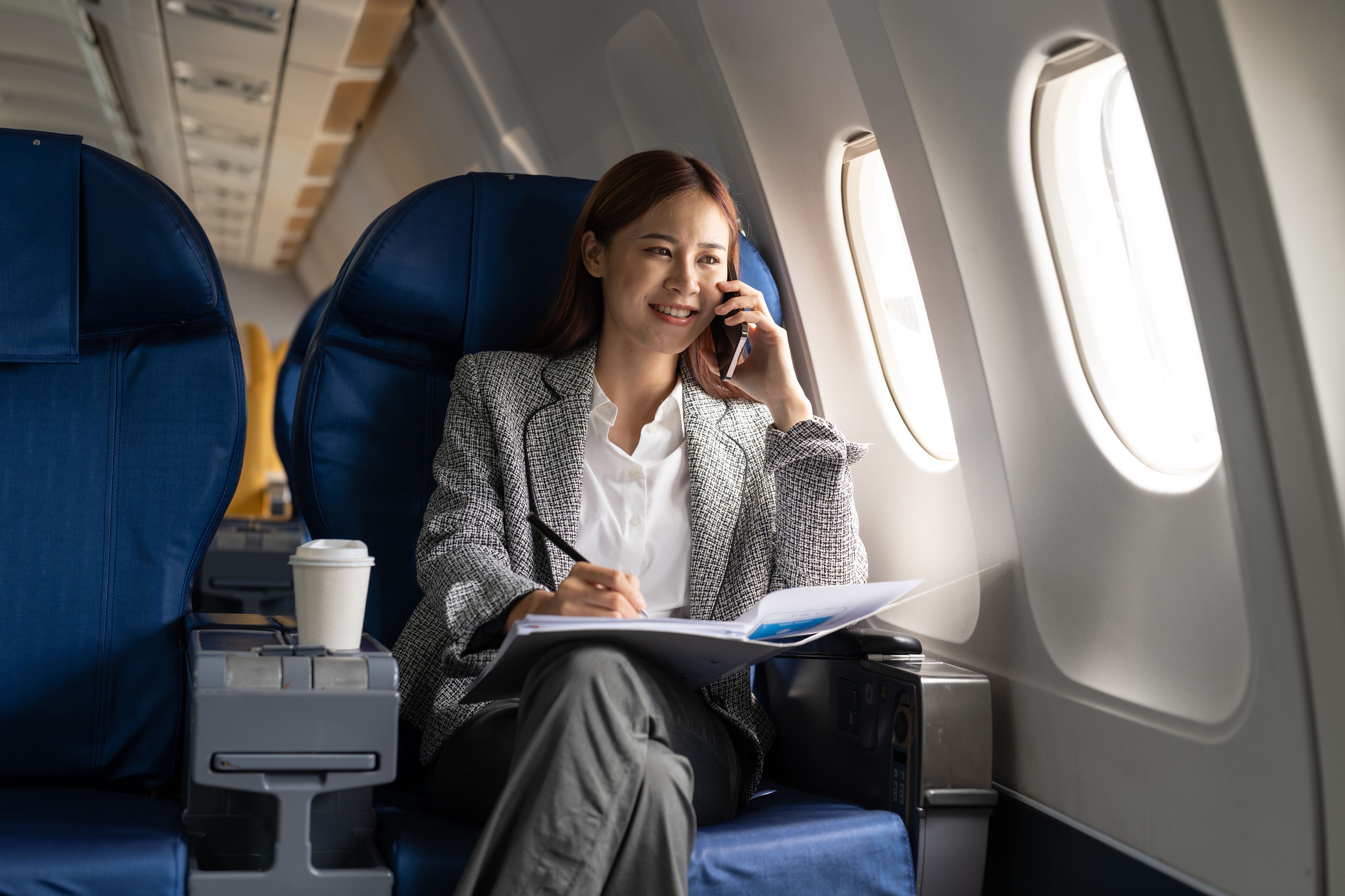 A Woman calling someone from her airplane seat.