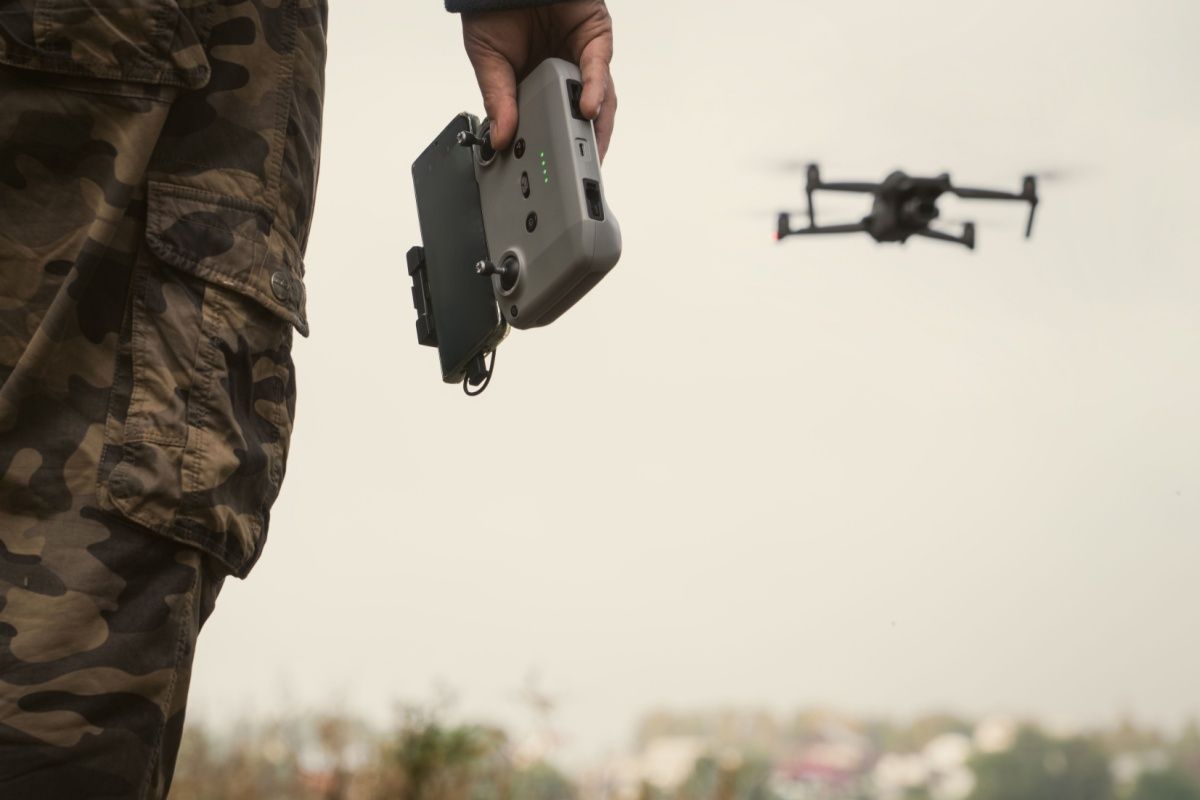 Man in a military uniform with a UAV control panel, a drone flying in the background