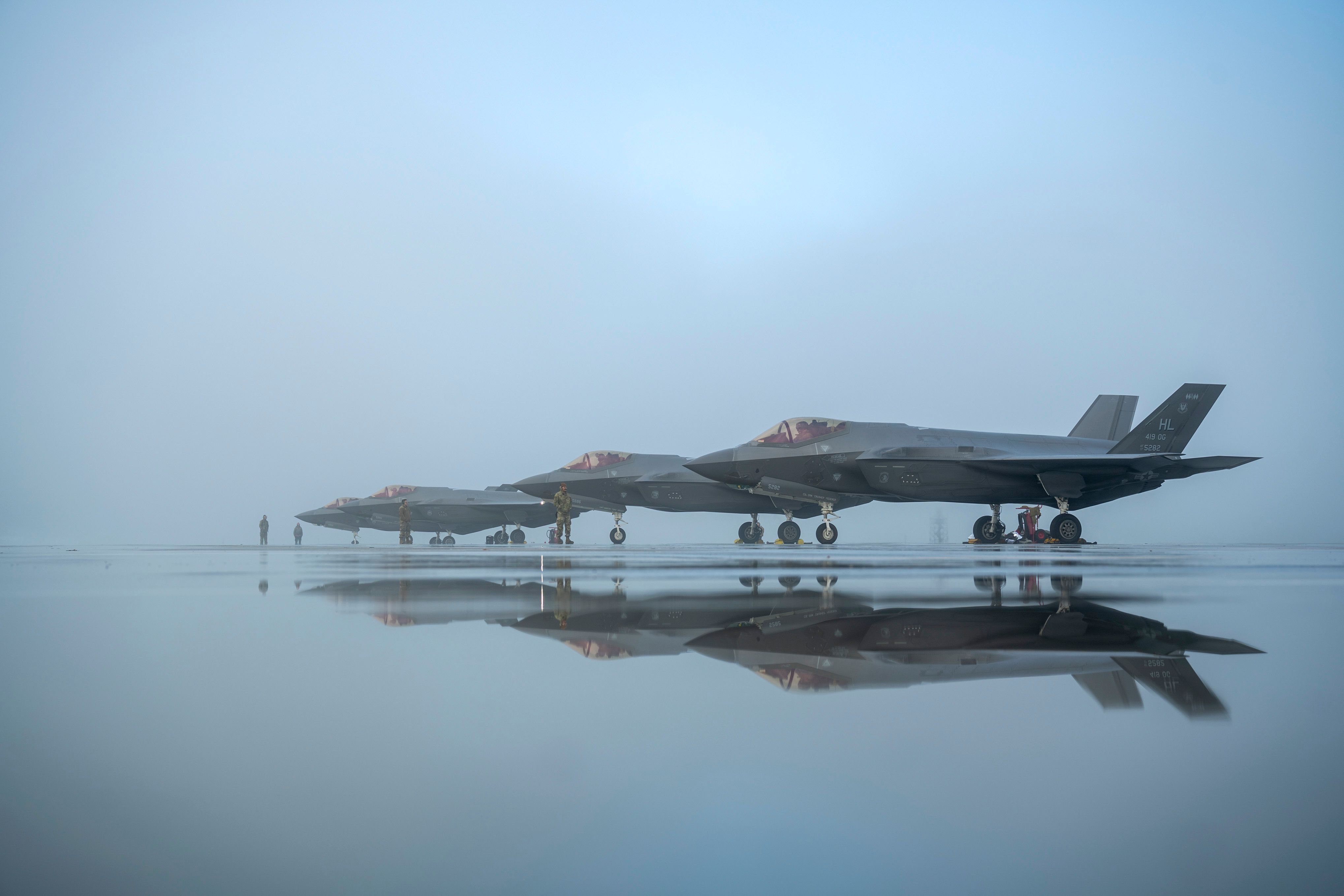 Three Lockheed Martin Lightning II parked on an airfield apron during foggy conditions.