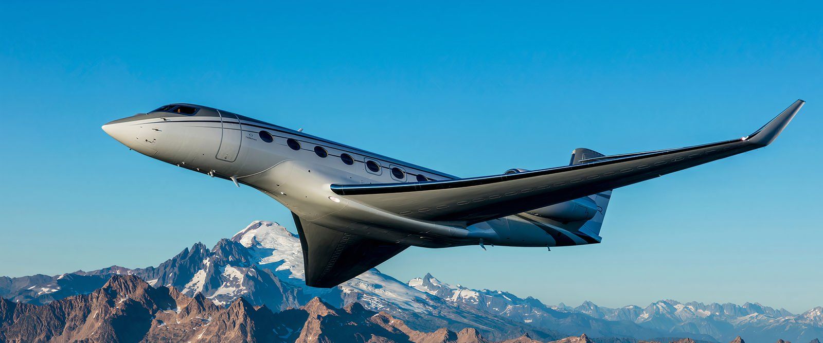 A G650ER in flight with mountains in the background.