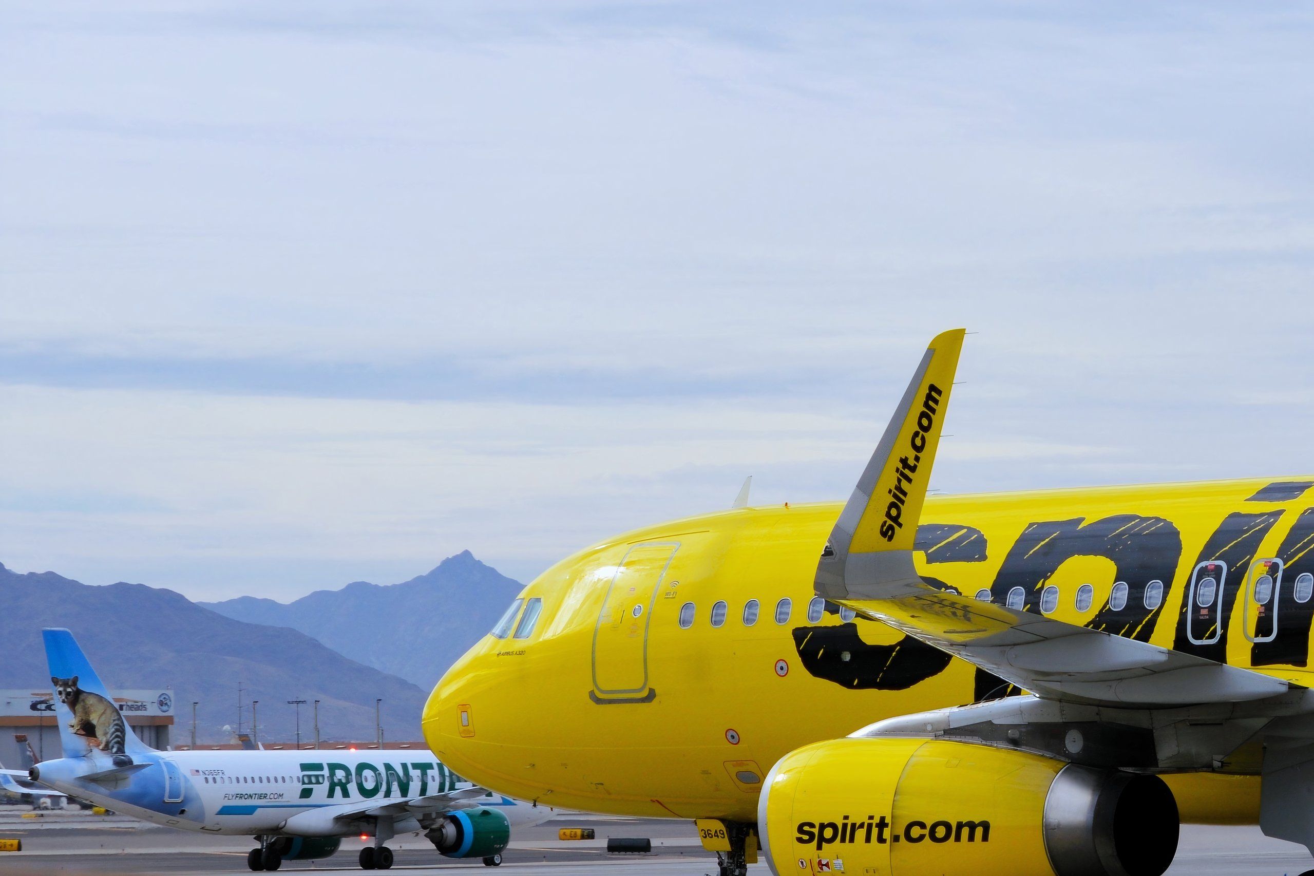 A bright yellow Spirit Airlines Airbus A320 passenger jet departs from Phoenix Sky Harbor International Airport (PHX) with a Frontier Airlines plane in the background