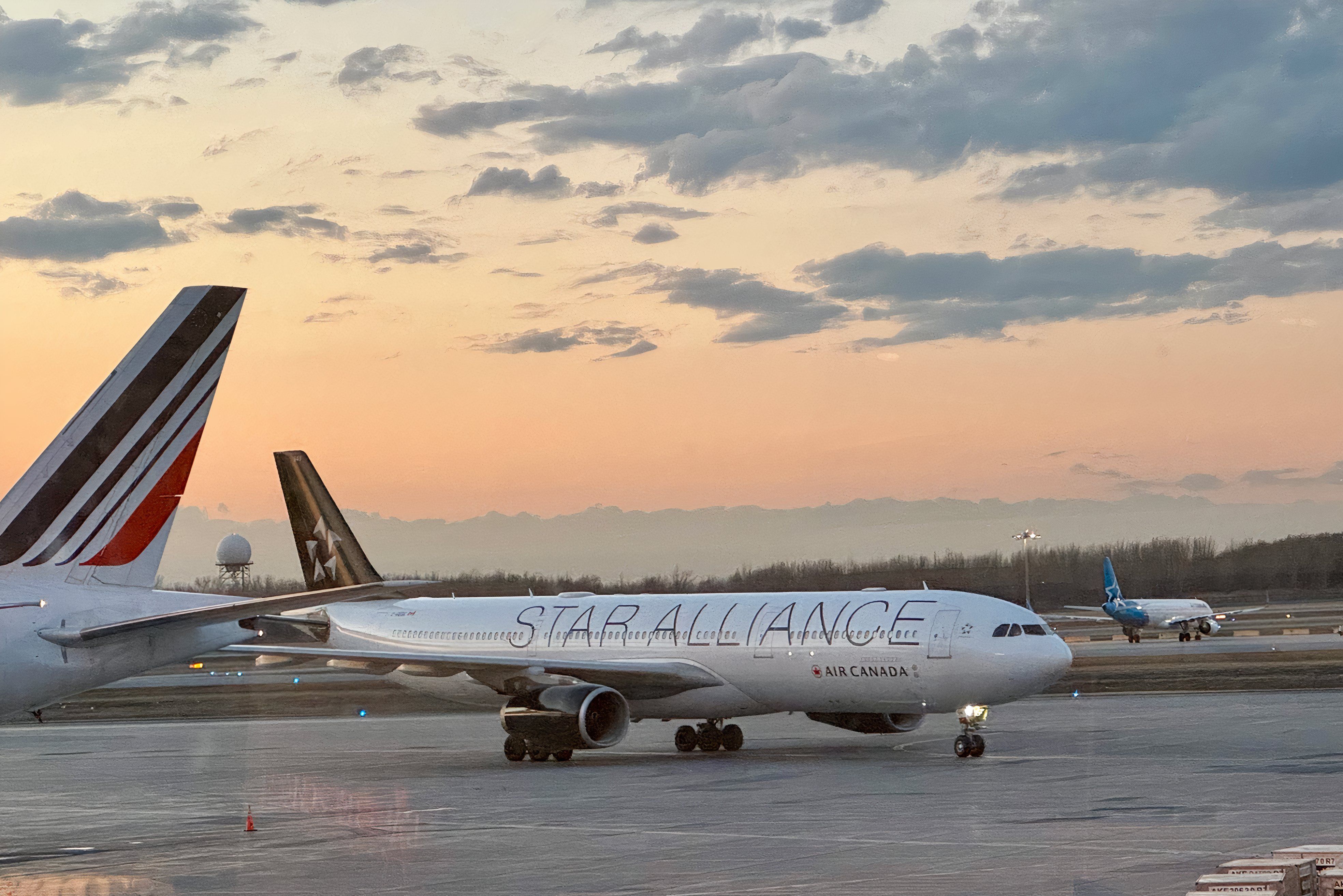 An Air Canada plane in the Star Alliance livery next to and Air France and Air Transat in the background