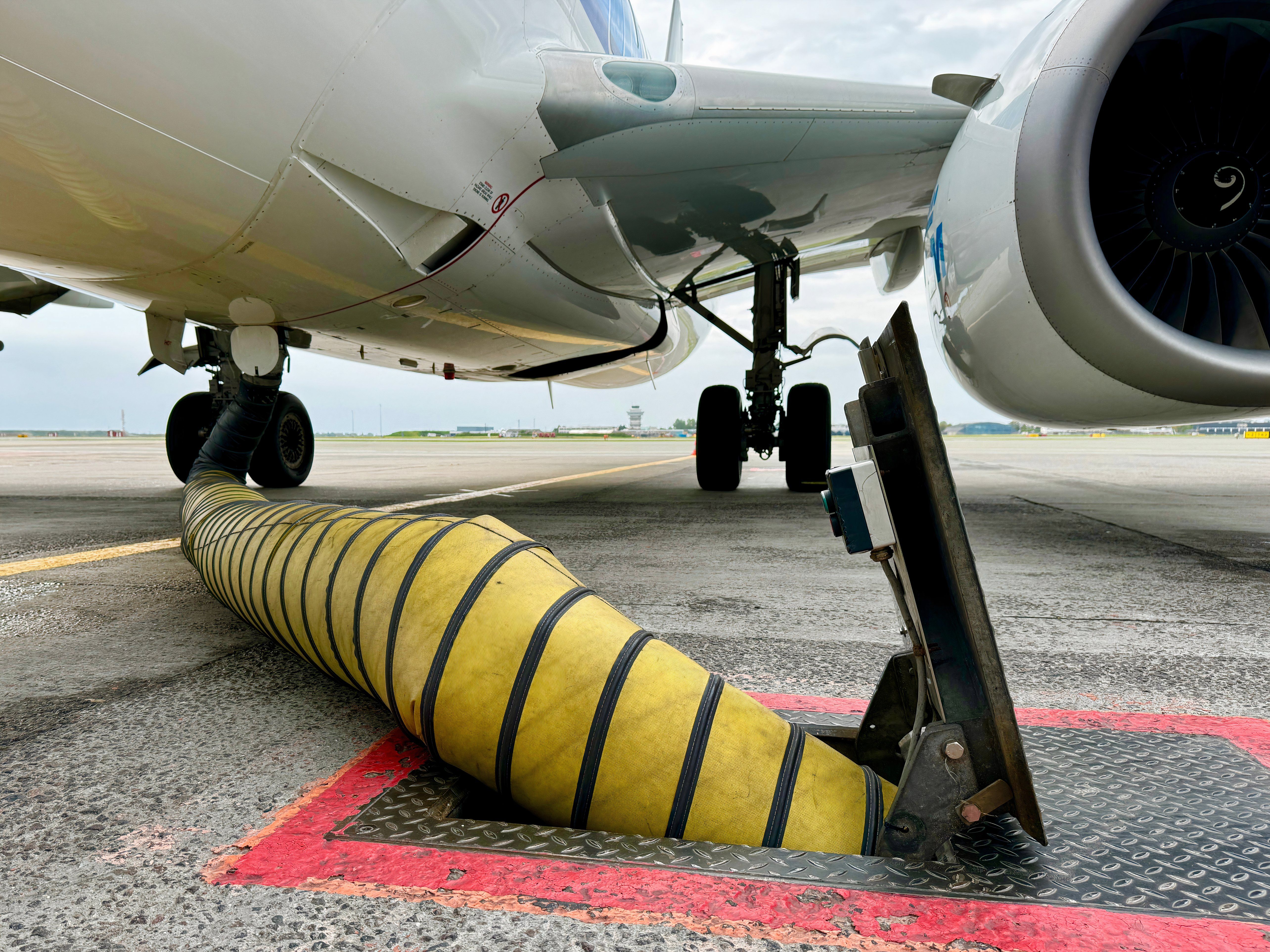 Yellow cooling airconditioning hose or pipe out of tarmac ground point with red lines connected to underside of airplane